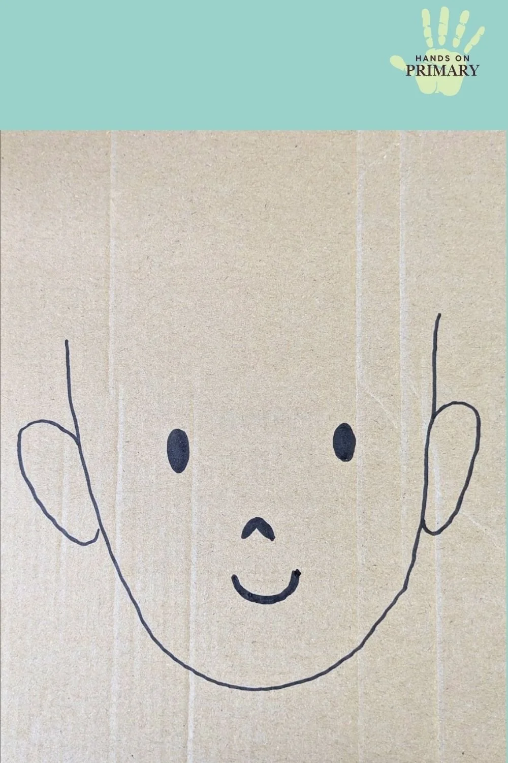 A cardboard face with no hair drawn in black marker on cardboard.