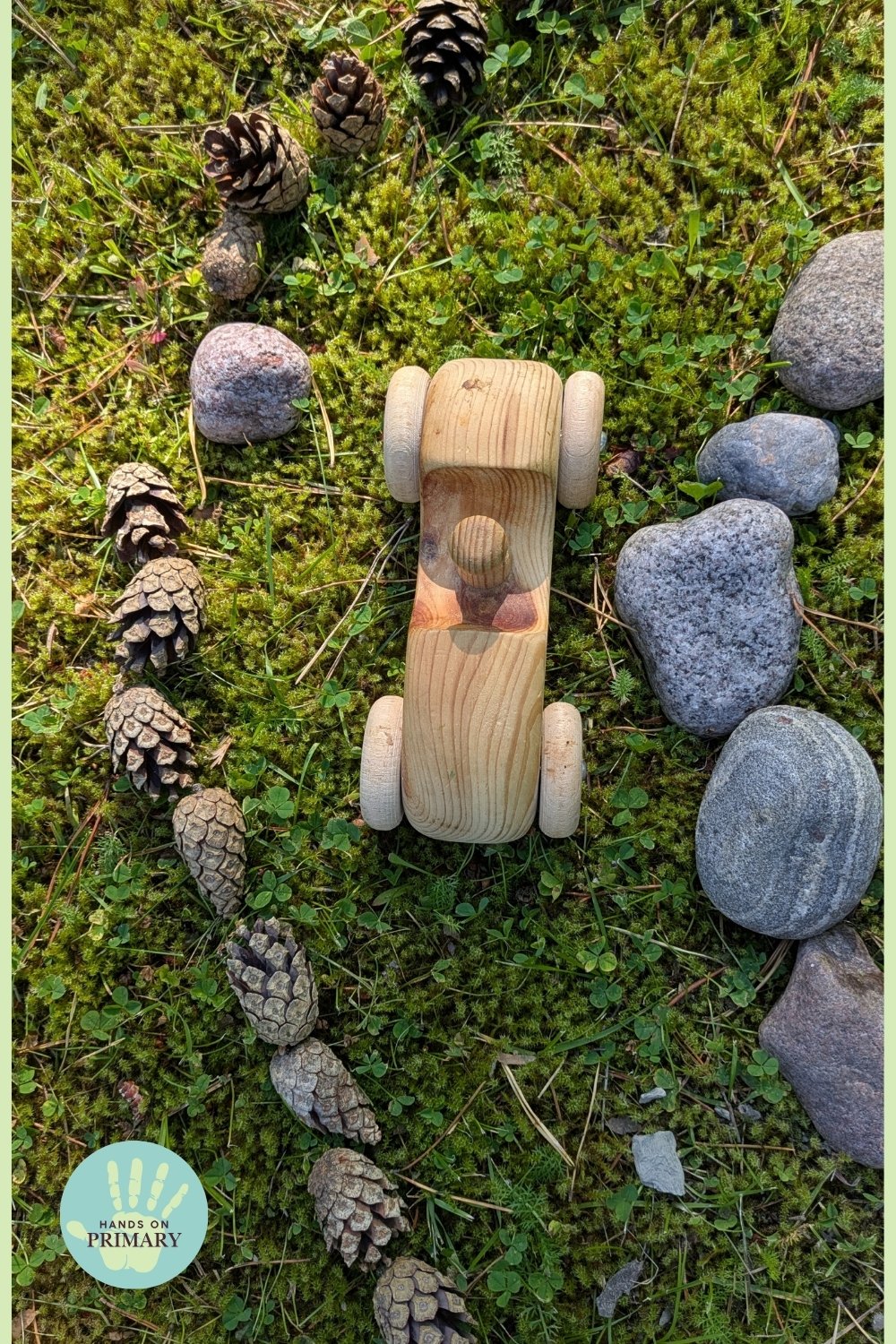Wooden toy car on a homemade outdoor racetrack created with stones and pine cones on grass.