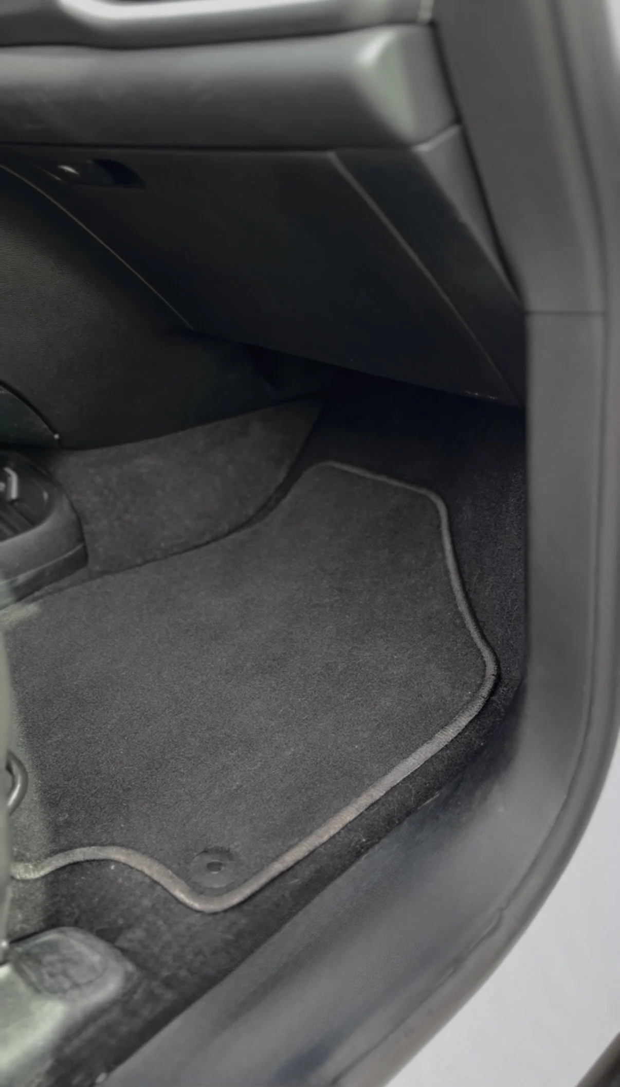 Car footwell with black floor mat and part of the dashboard visible.