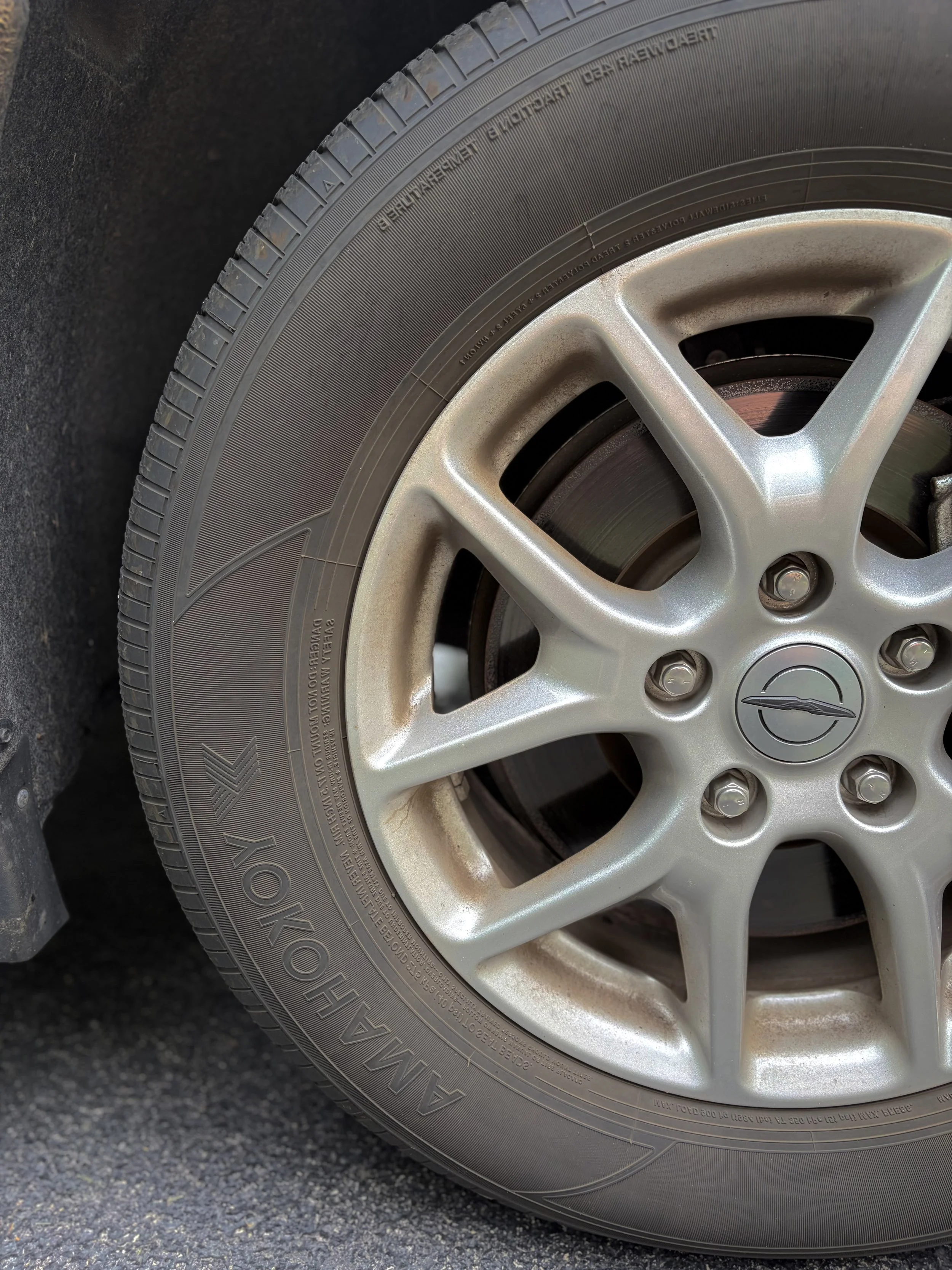 Close-up of a car tire with the silver alloy wheel showing on a dark asphalt surface.