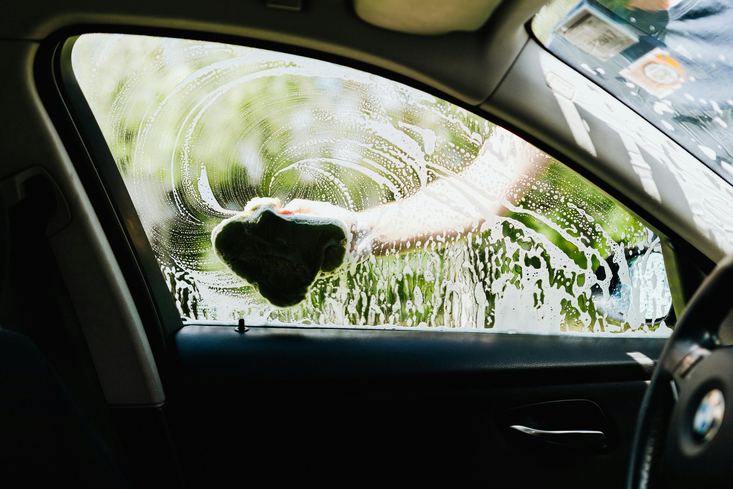 Car windshield being cleaned with a cloth, with soap and foam on the glass.