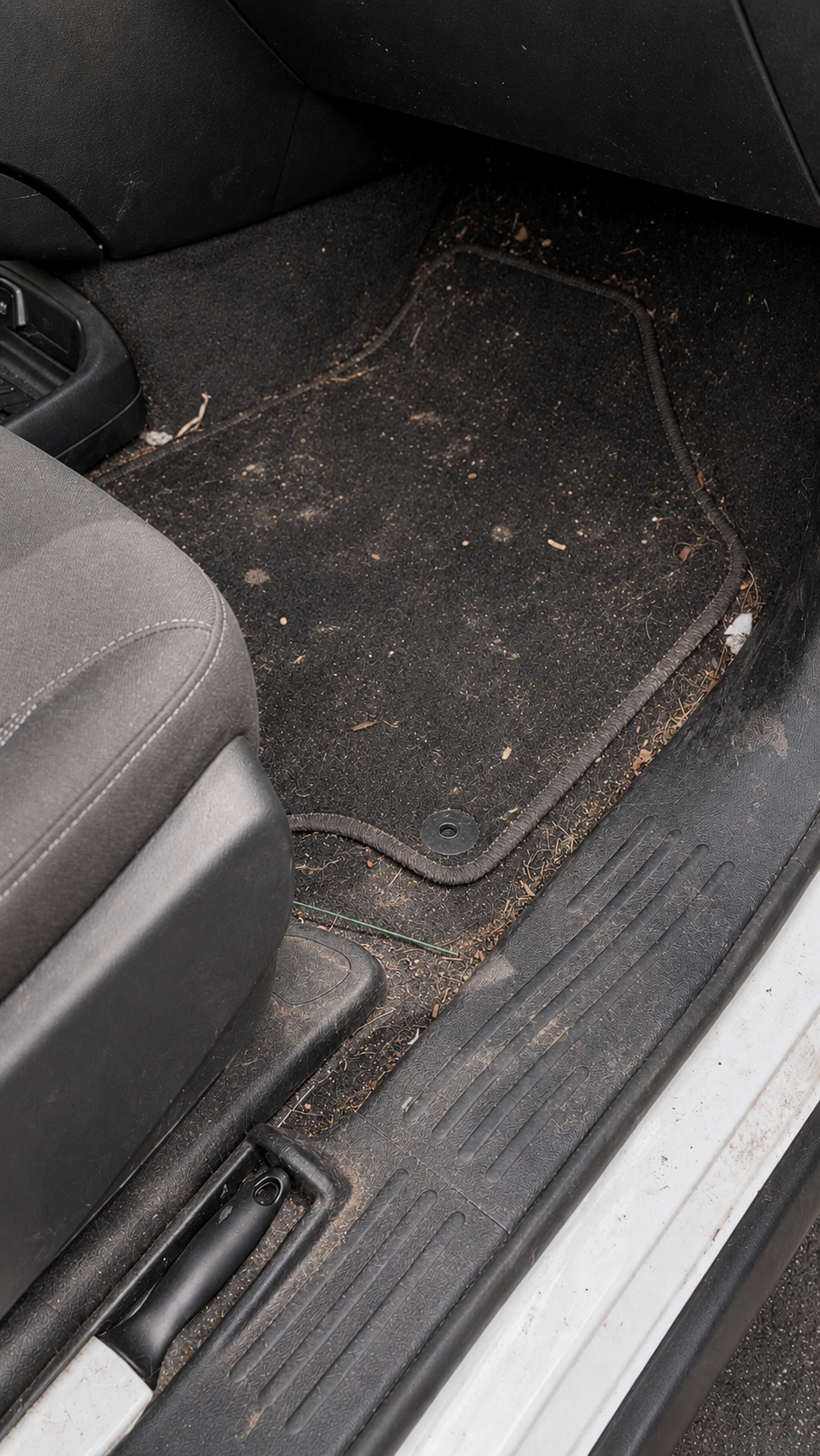 Dirty black car floor mat and scuffed door sill in a vehicle interior.