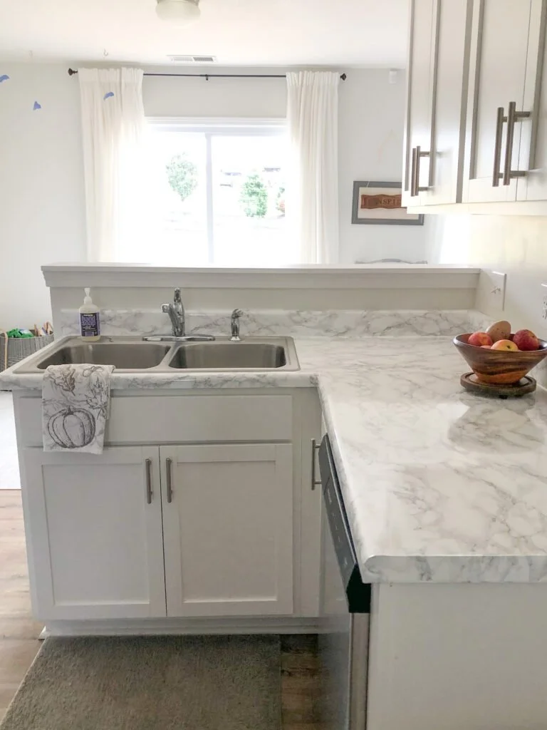  Kitchen after phase 1 changes, a vinyl product to cover the brown counters, a painted wood piece instead of the brown counter behind the sink, the cabinets are still white,  