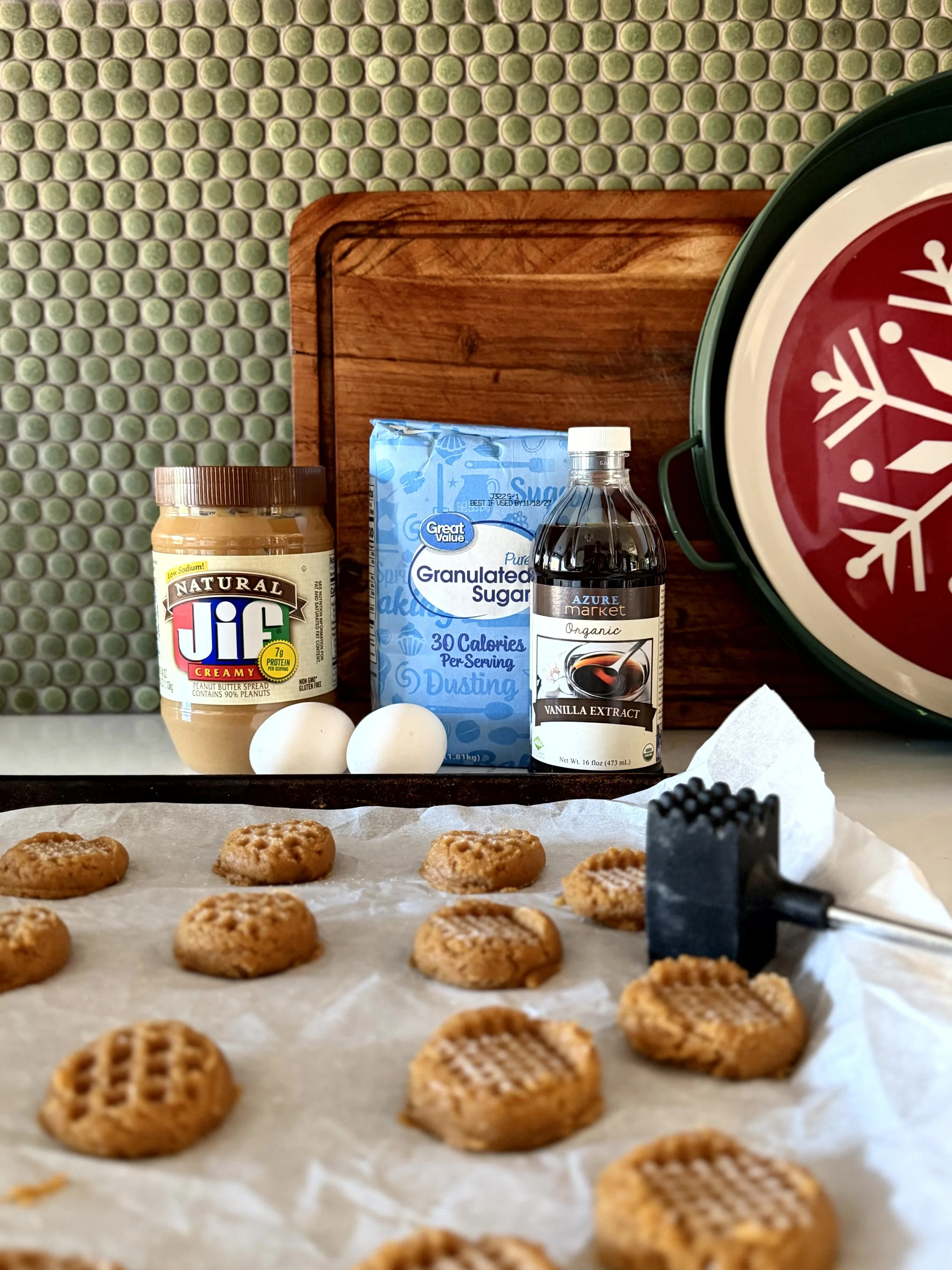 uncooked peanut butter cookies on a parchment lined cookie sheet, ingredients for these cookies are behind the cookie sheet, setting is in a cozy kitchen decorated for christmas