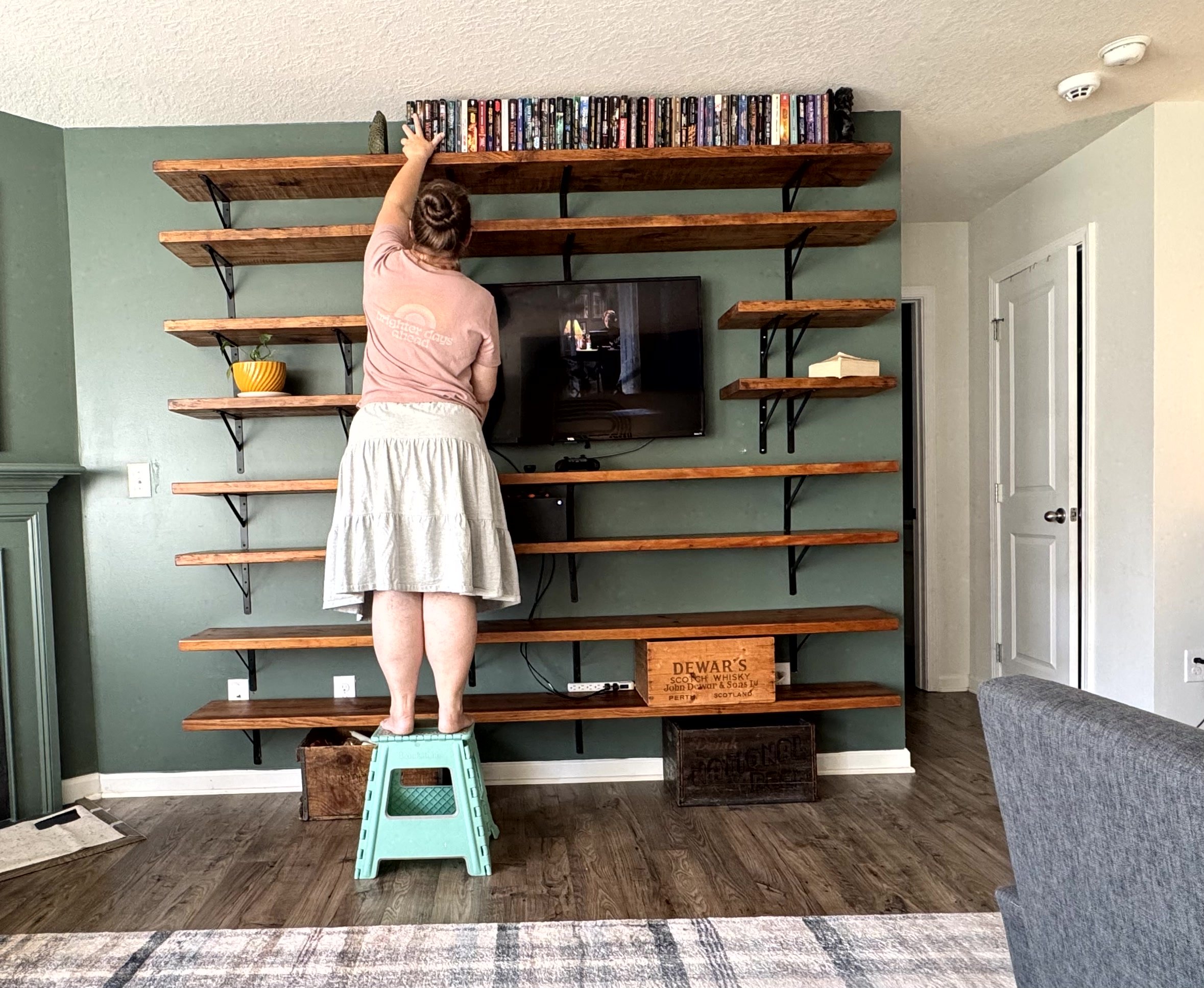 Another shot of the woman putting books up on the top shelf of the new installed shelves. She is watching the classic rom-com, You’ve got Mail on the TV starring Meg Ryan and Tom Hanks.  
