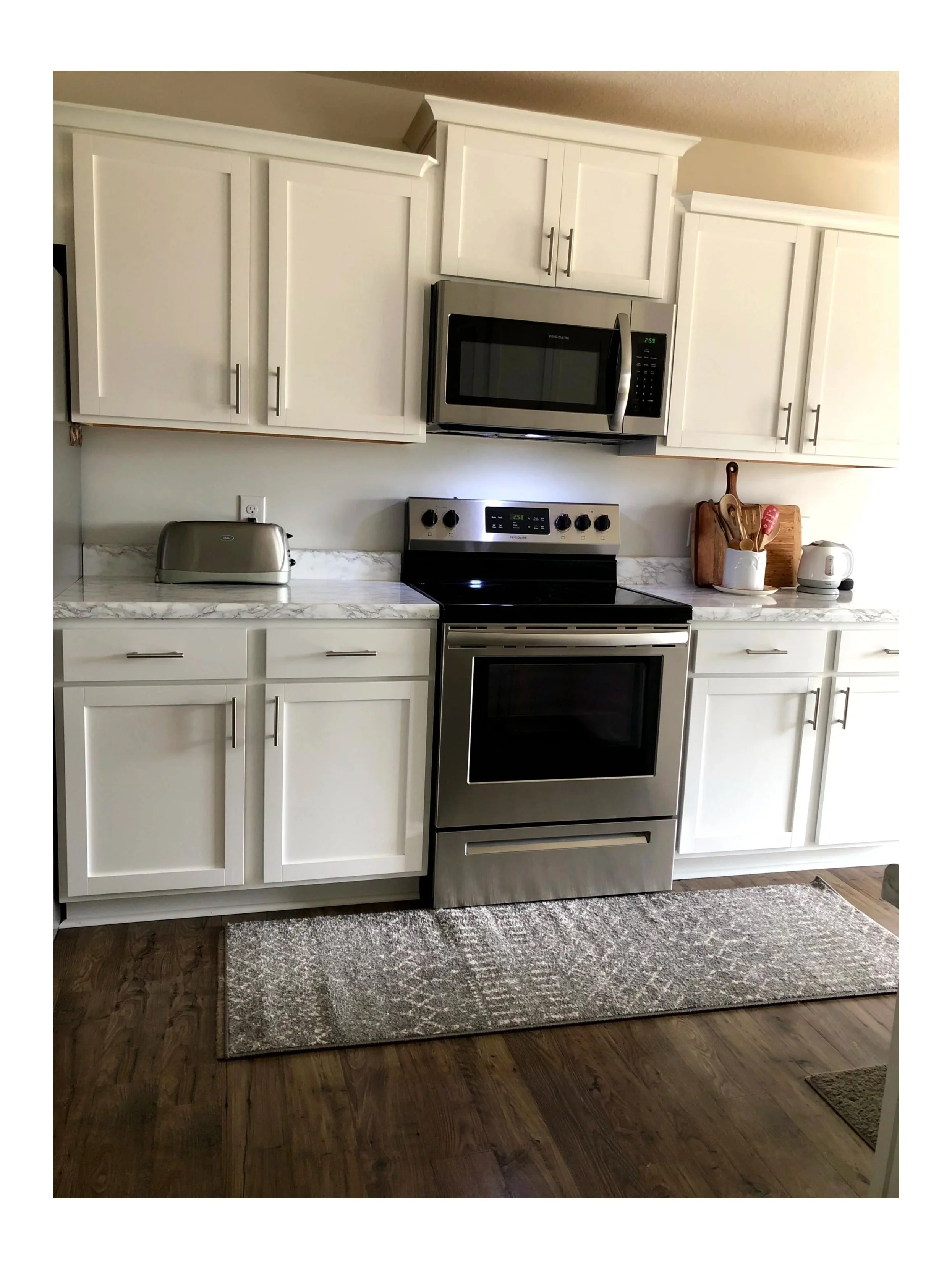 Kitchen with microwave over the stove, both stainless, whtie cabinets, stainless toaster, and wood accents on the other side of the stove. Medium tone lvp floors.  