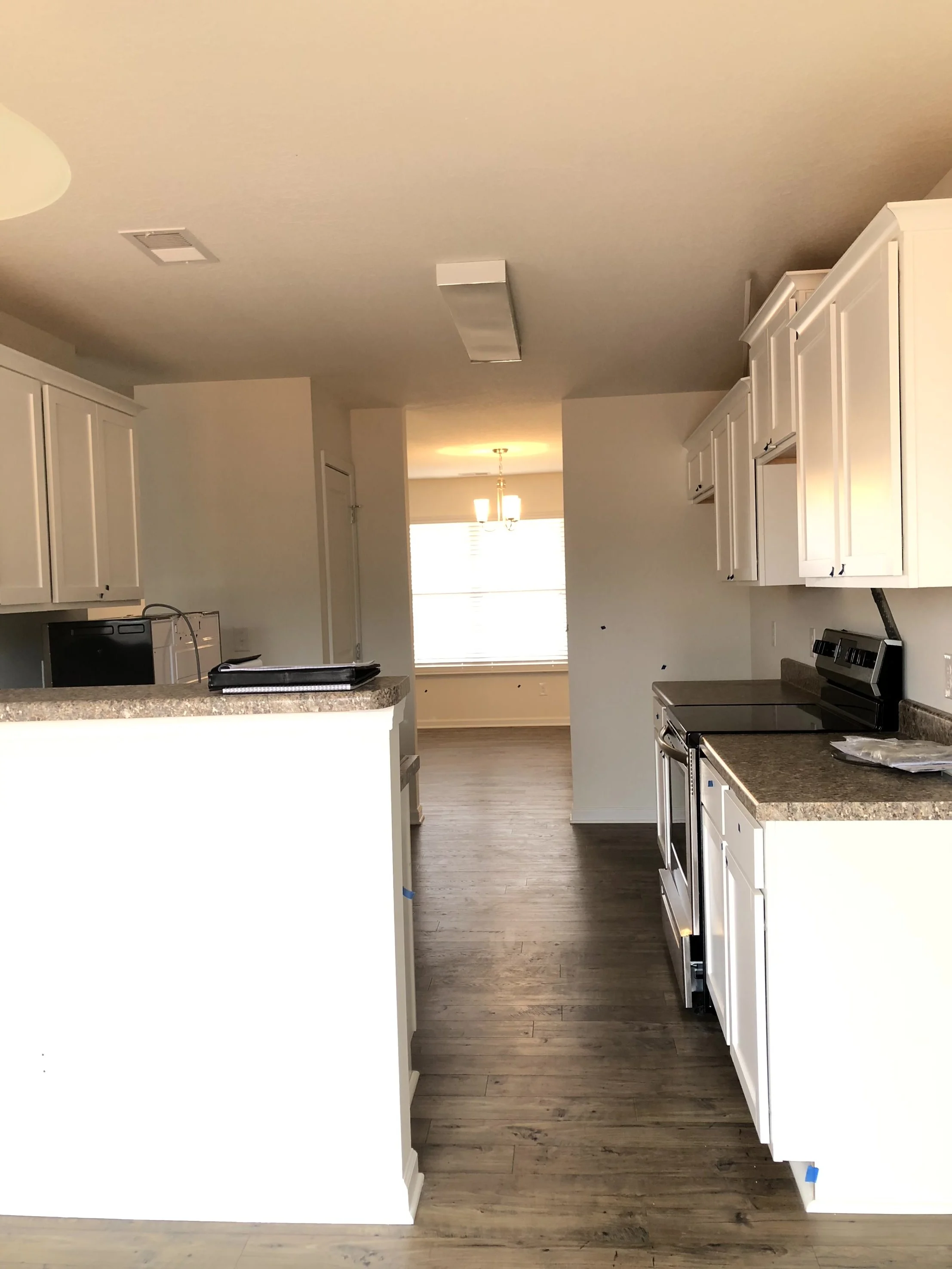 kitchen pre renovation, brown counters, whtie cabinets, dining room visible but empty through doorway