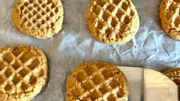 peanut butter cookies with a pattern from a meat tenderizer imprinted on them; laying on parchment paper