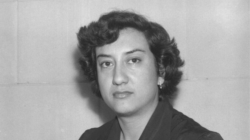 Retrato en blanco y negro de una mujer con cabello rizado y vestido oscuro, mirando hacia la cámara.