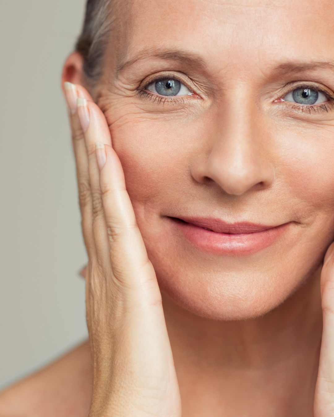 Close-up of a woman gently touching her face, smiling softly, with clear skin and blue eyes.