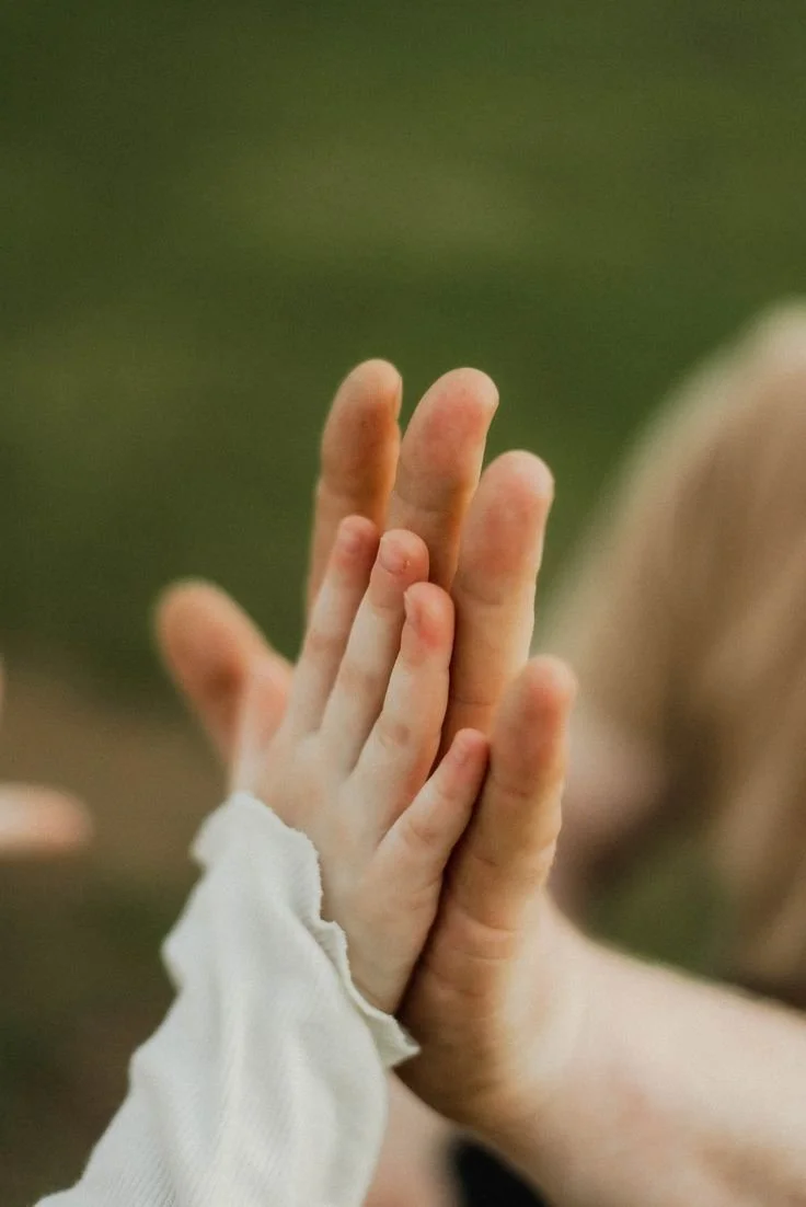 Close-up of an adult's hand gently holding a child's hand during a high five.