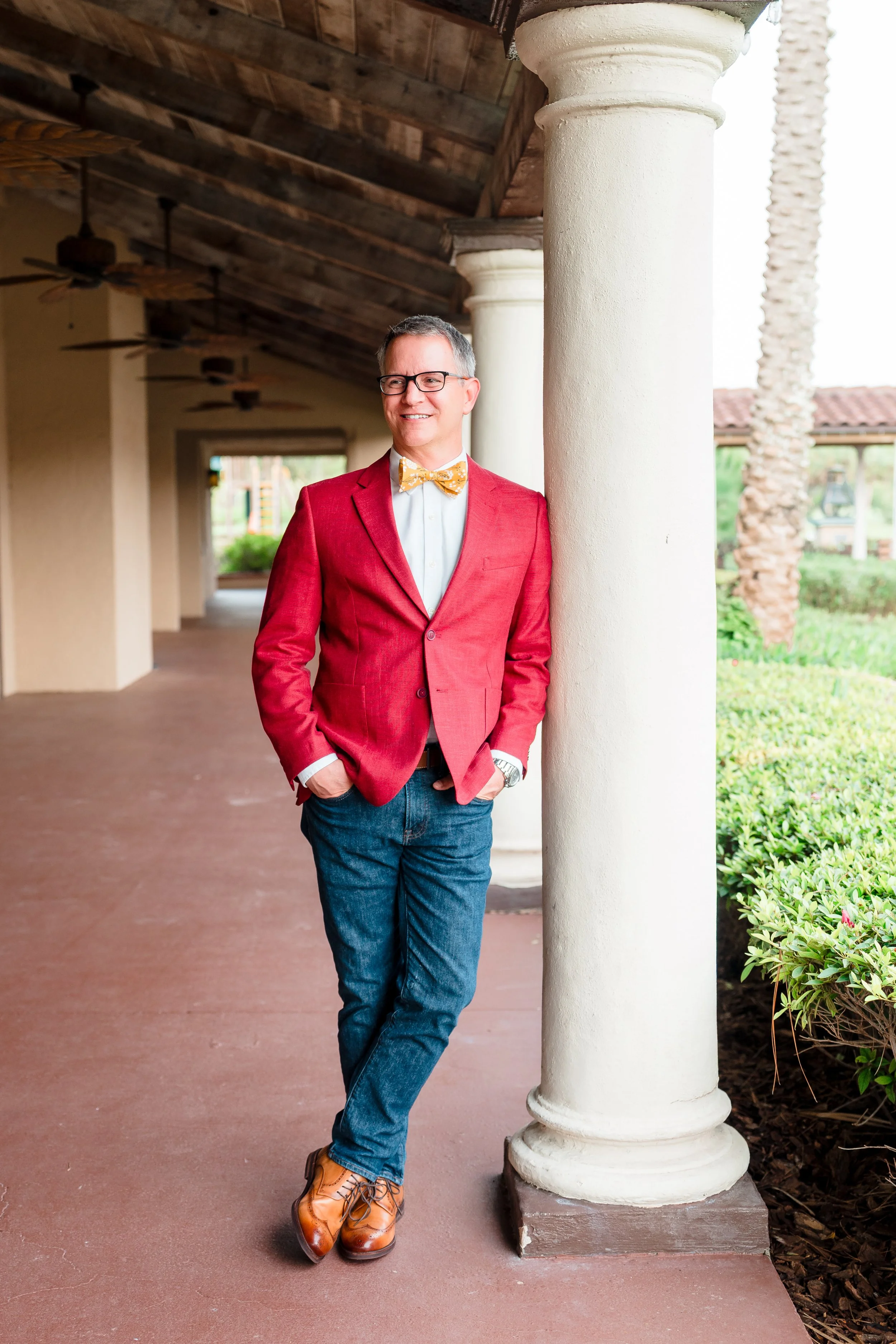 Guy Swenson Ed.D. founder of Index & Atlas leaning against a column at Mission Inn Resort + Club in Howey-in-the-Hills, Florida wearing a red jacket and gold bow tie