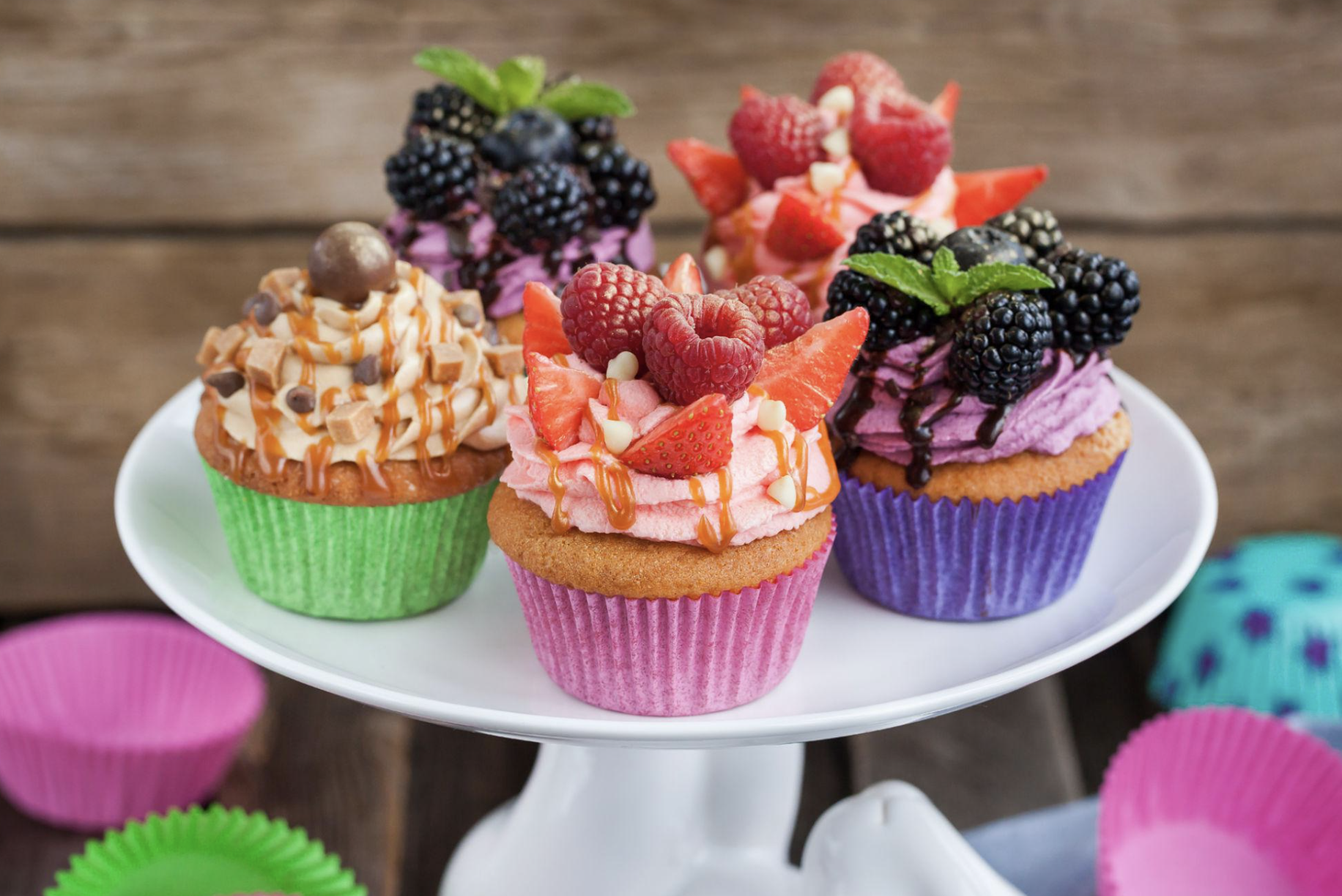 Assorted colorful cupcakes topped with berries and garnishes on a white cake stand.