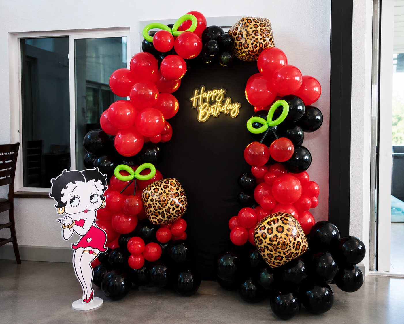 Decorative Betty Boop birthday party backdrop with balloons, a neon "Happy Birthday" sign, a Betty Boop cardboard cutout, and leopard print balloon accents.