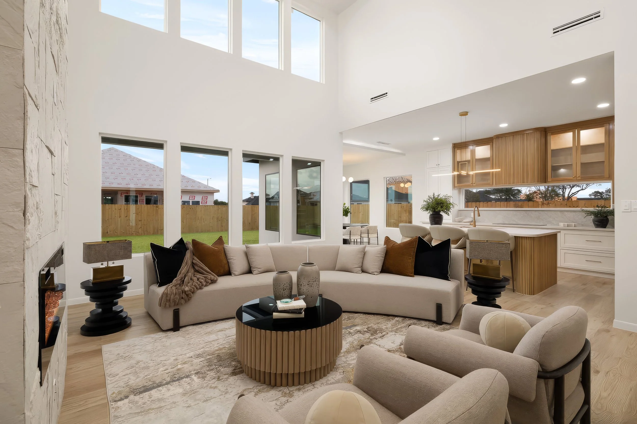 Spacious, modern living room with large windows, beige sofas, and decorative vases, featuring a high ceiling and view of backyard.