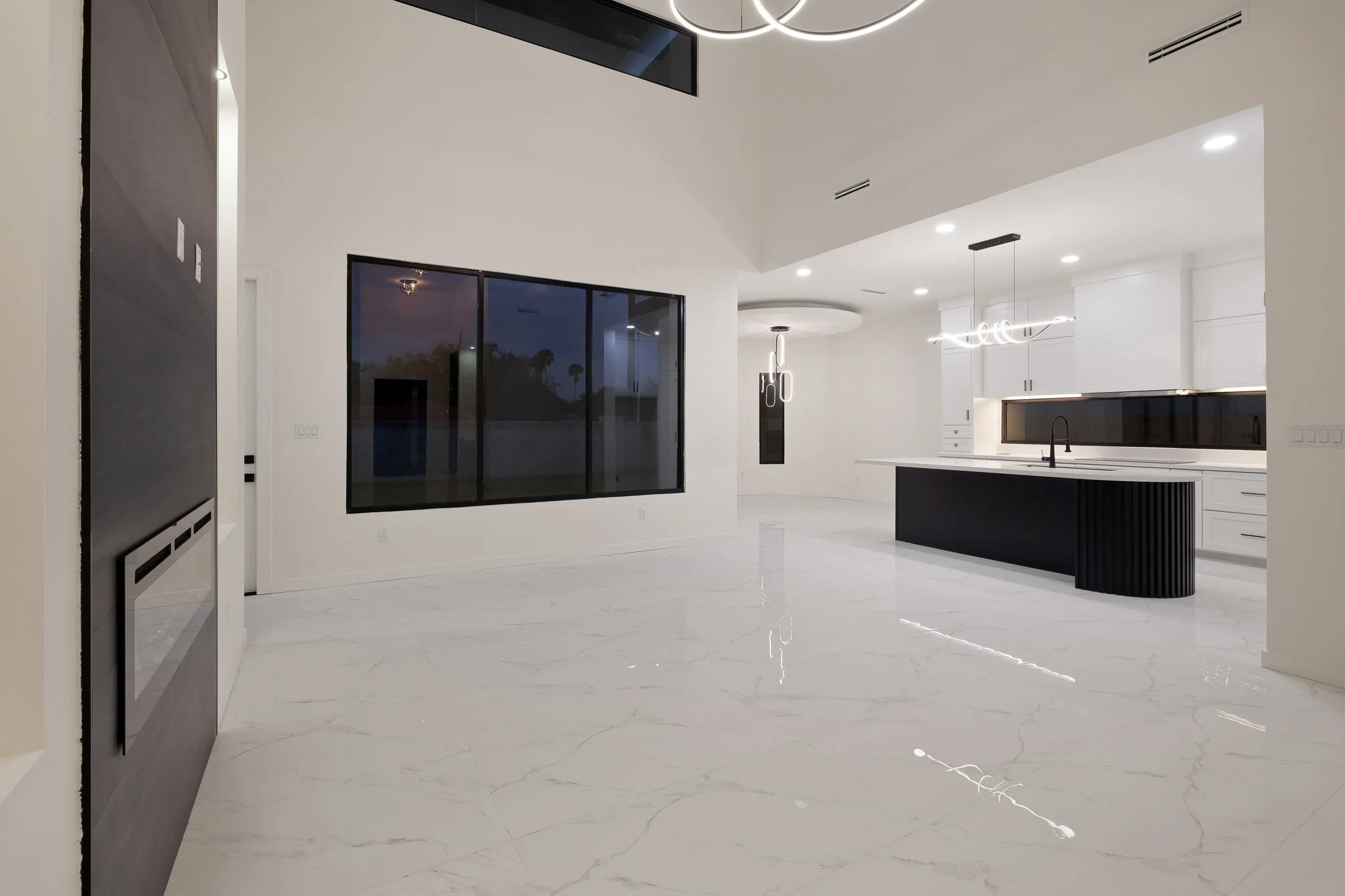 Modern kitchen with white cabinets, black island, marble floors, large sliding glass doors, and minimalistic lighting fixtures.