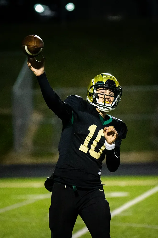 Football quarterback in a yellow helmet and black jersey throwing a pass under stadium lights