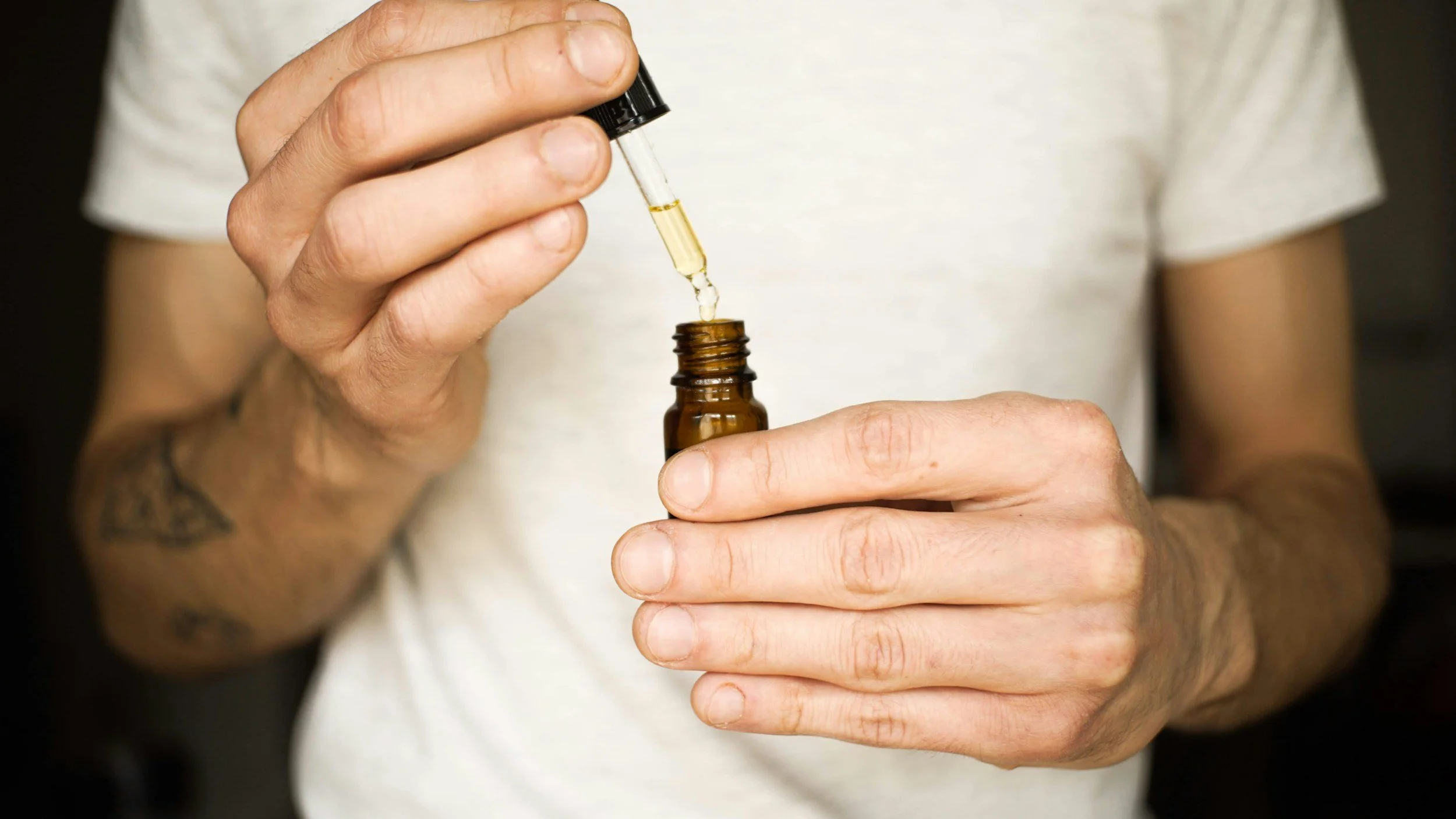 Person holding a small amber glass bottle with a dropper, dispensing a clear yellow liquid.