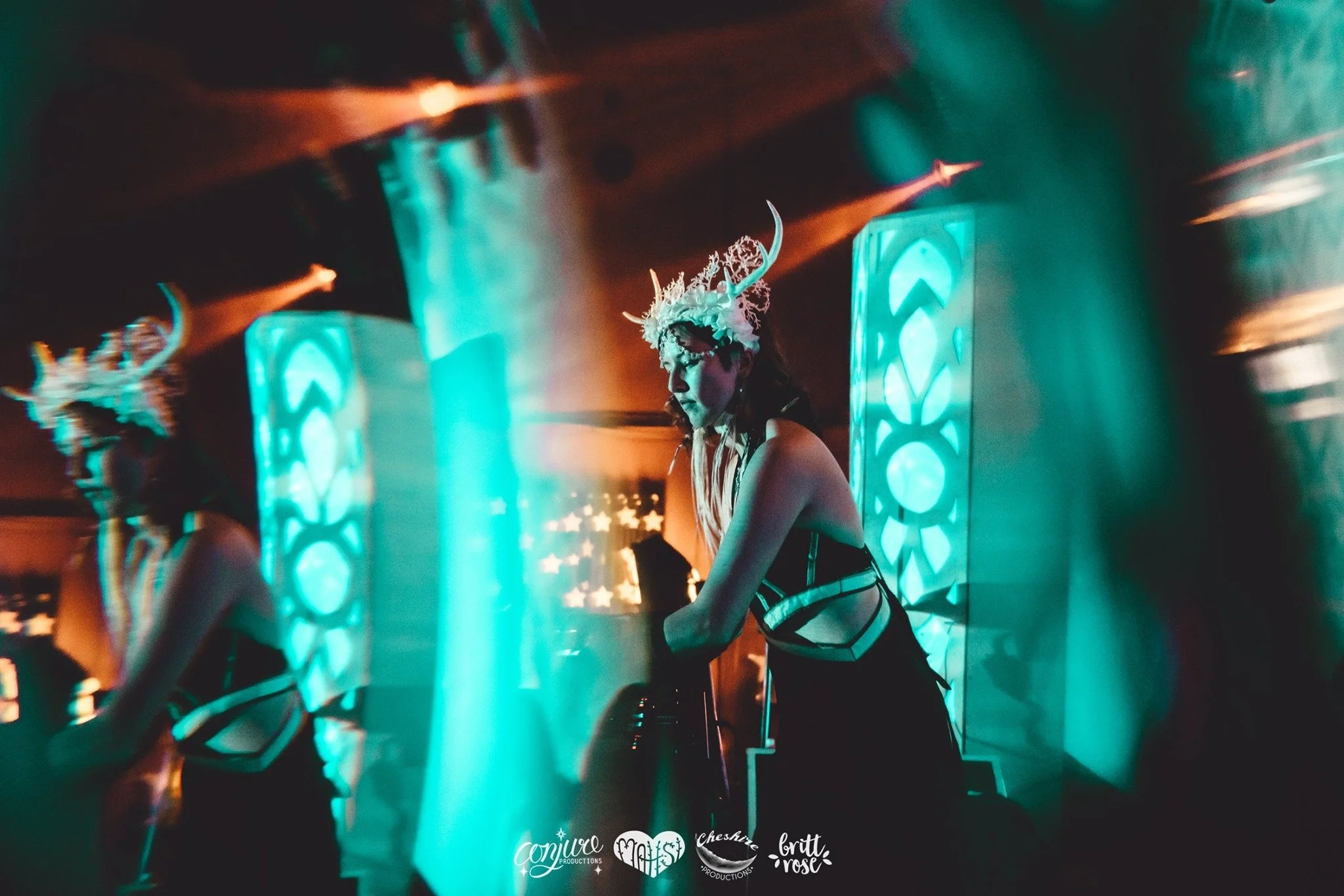Kylee Dawn performing at Inshala/Souluna wearing a decorative headpiece with antlers and flowers, performing on stage with colorful LED lights and electronic equipment in the background.