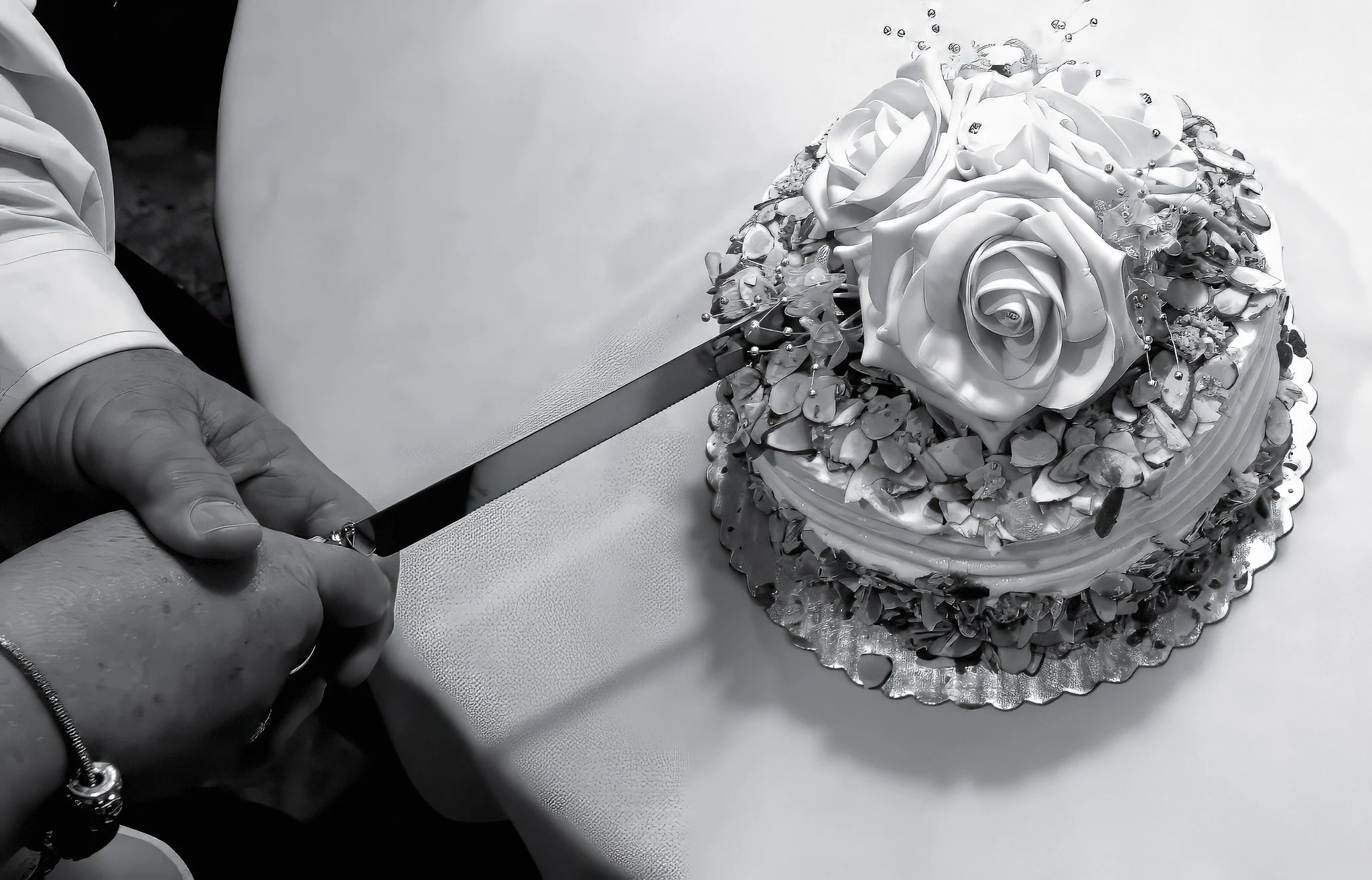 A person wearing gloves is decorating a round cake with white roses and silver embellishments.