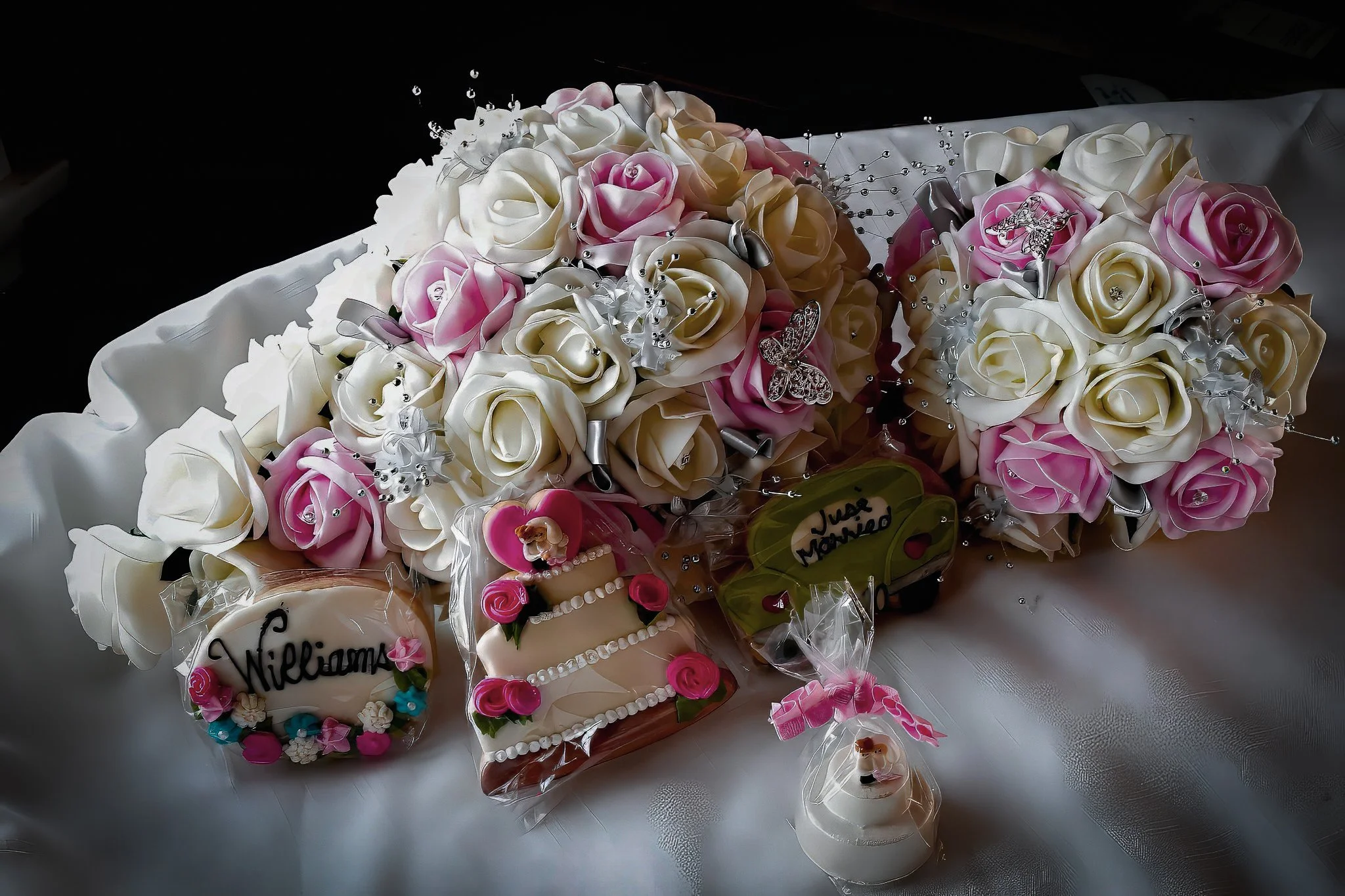 A bouquet of pink and white artificial roses with decorative rhinestones and ribbon accents, placed on a white cloth surface.