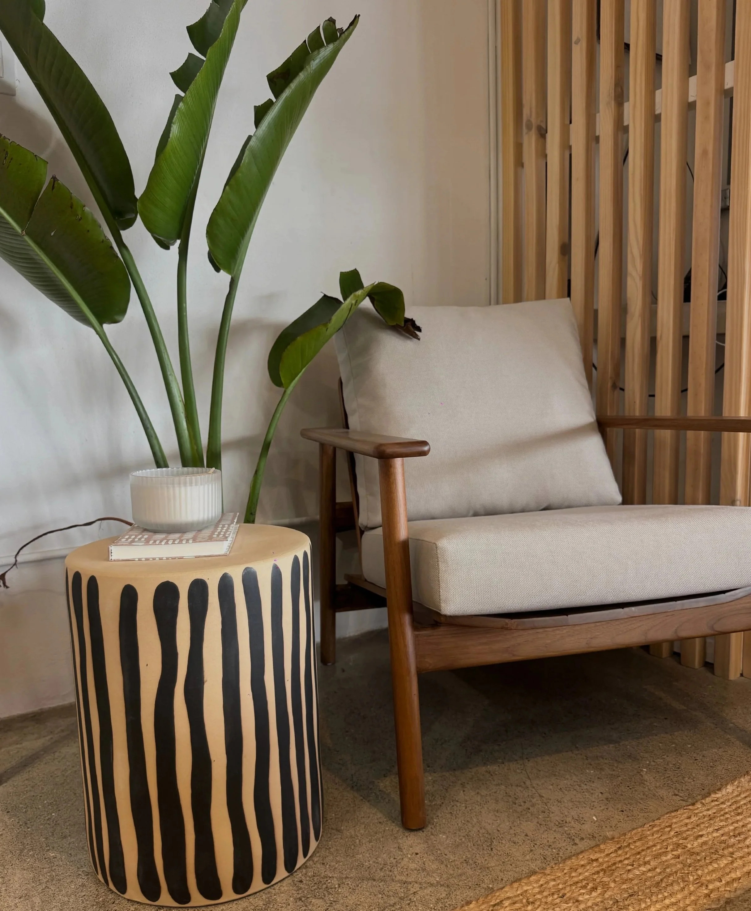 A styled interior with a potted plant, a coffee table with books and a lamp, a beige armchair, and a wooden room divider, by OLA Creative Studio