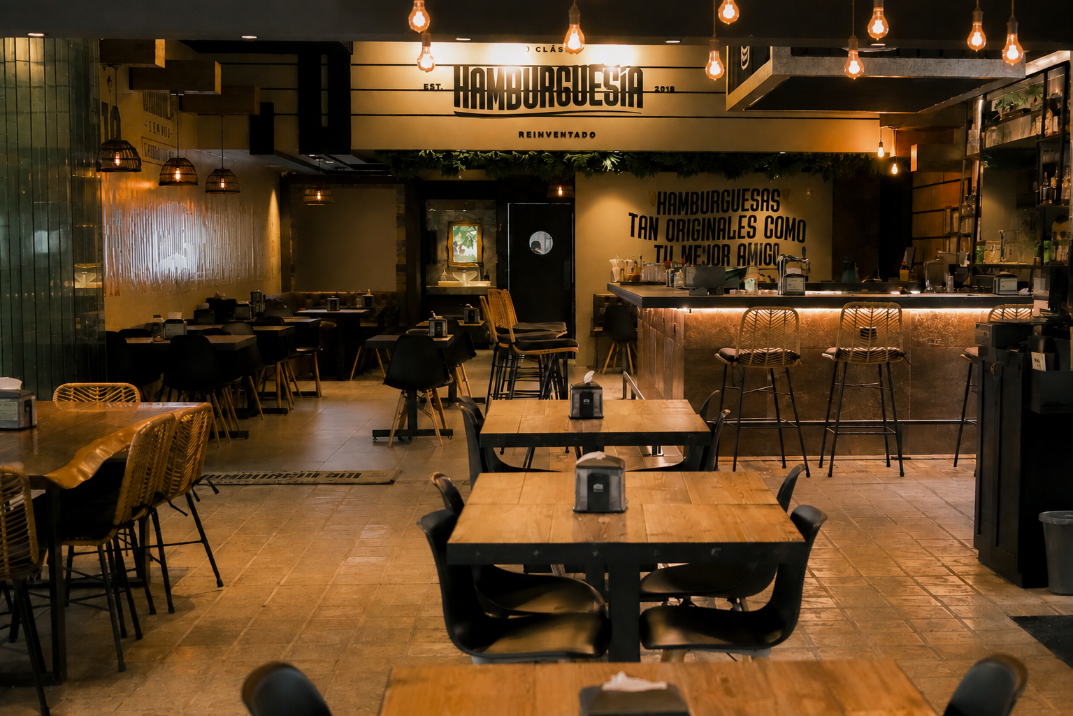 Interior of a warmly lit restaurant with wooden tables, a bar, and greenery, by OLA Creative Studio