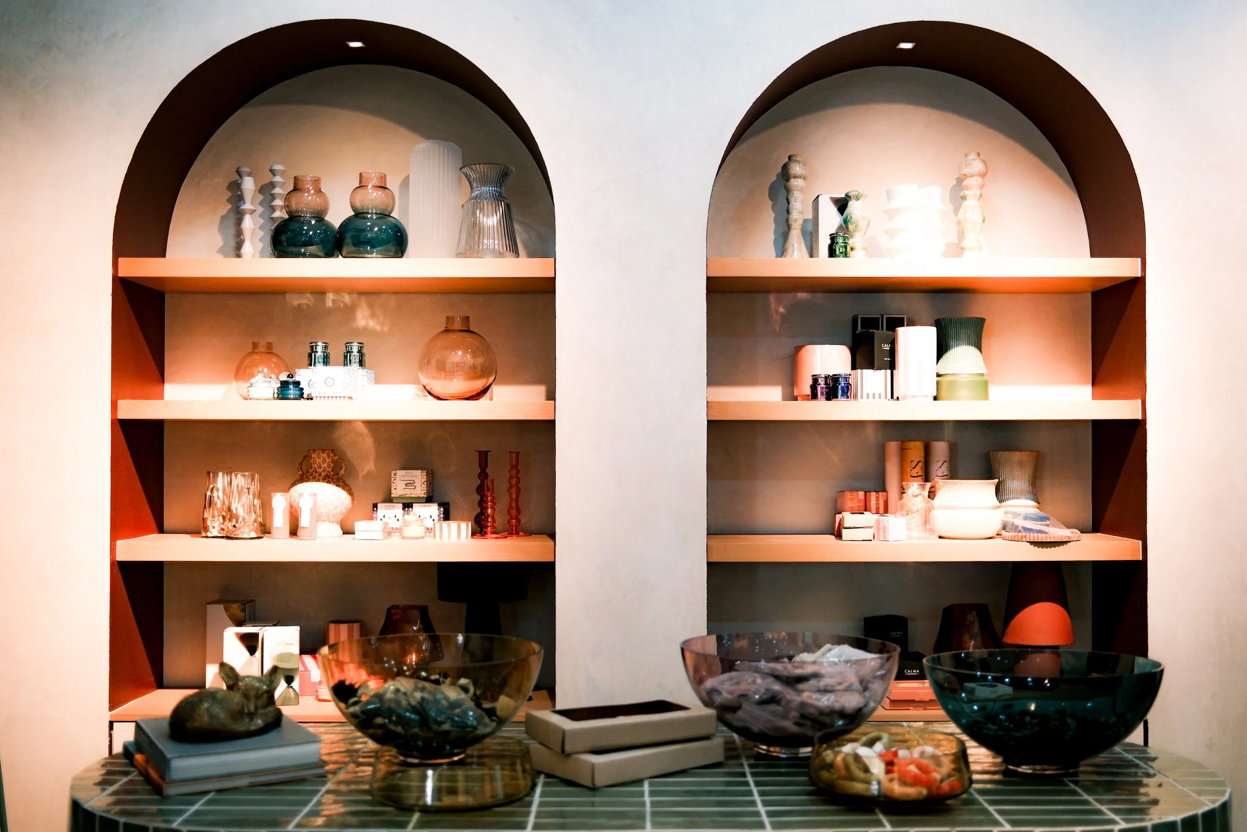 Display shelves of decorative vases, jars, and bottles beside a table of bowls and small decor items in Unikko, by OLA Creative Studio