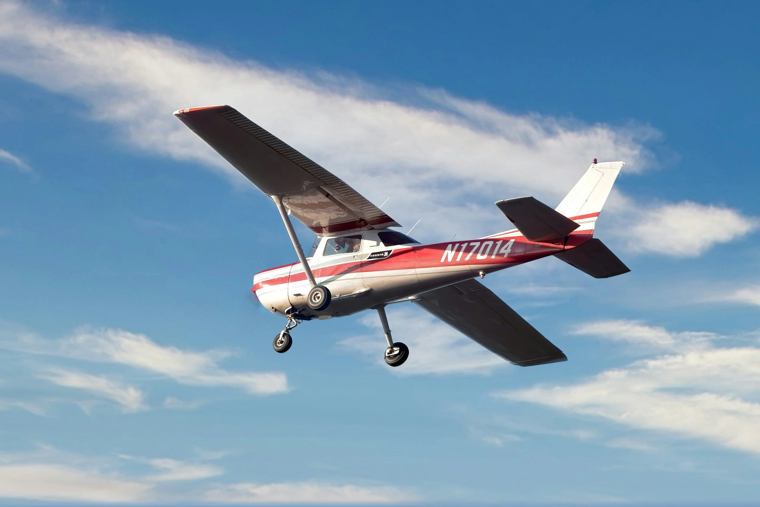 Small red and white single-engine airplane flying in the blue sky with white clouds.