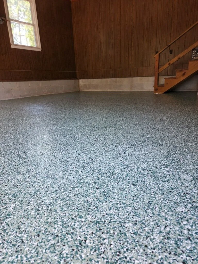 Empty room with wooden walls, a window letting in natural light, and speckled gray flooring.
