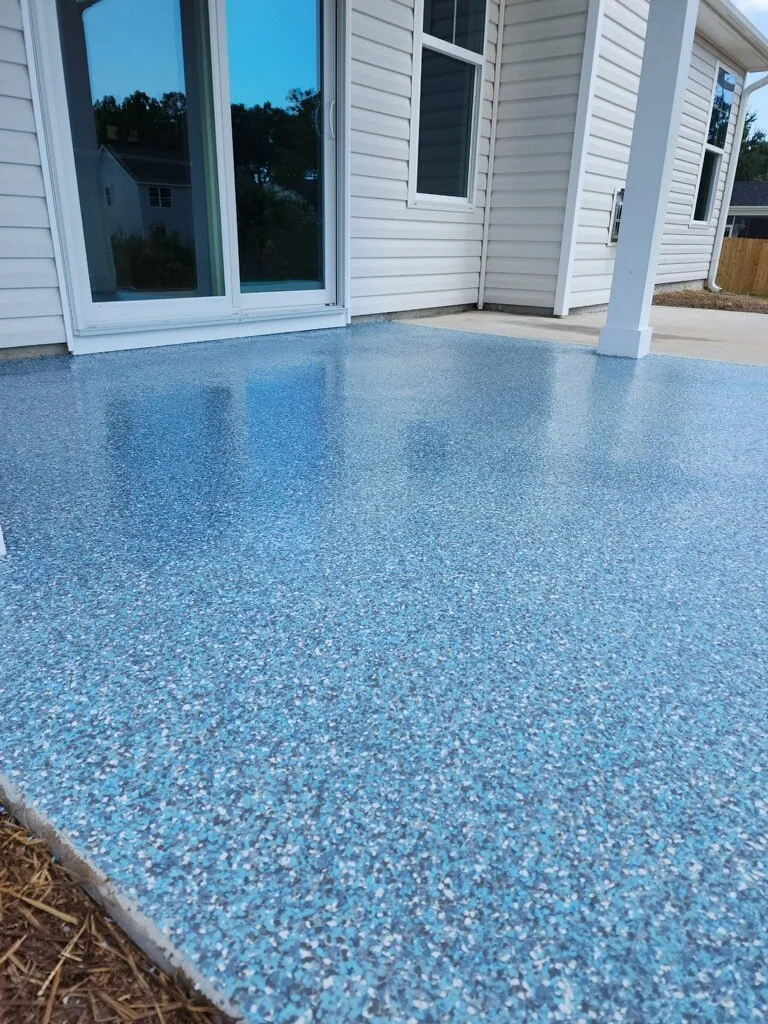 Newly poured blue epoxy porch flooring outside a white house with sliding glass door and window