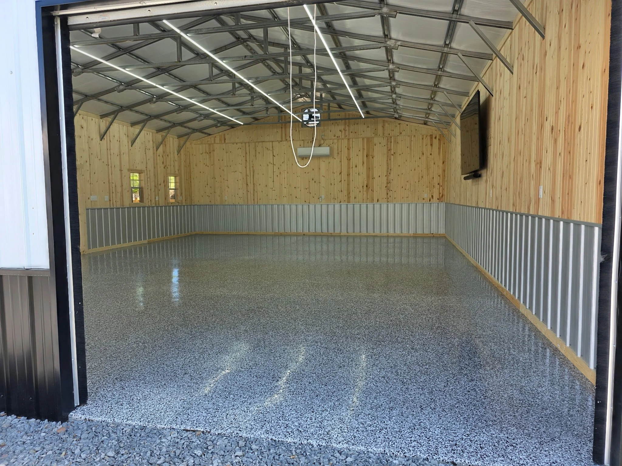 Empty garage with wooden walls, metal ceiling, and gray terrazzo flooring, viewed from the open garage door.