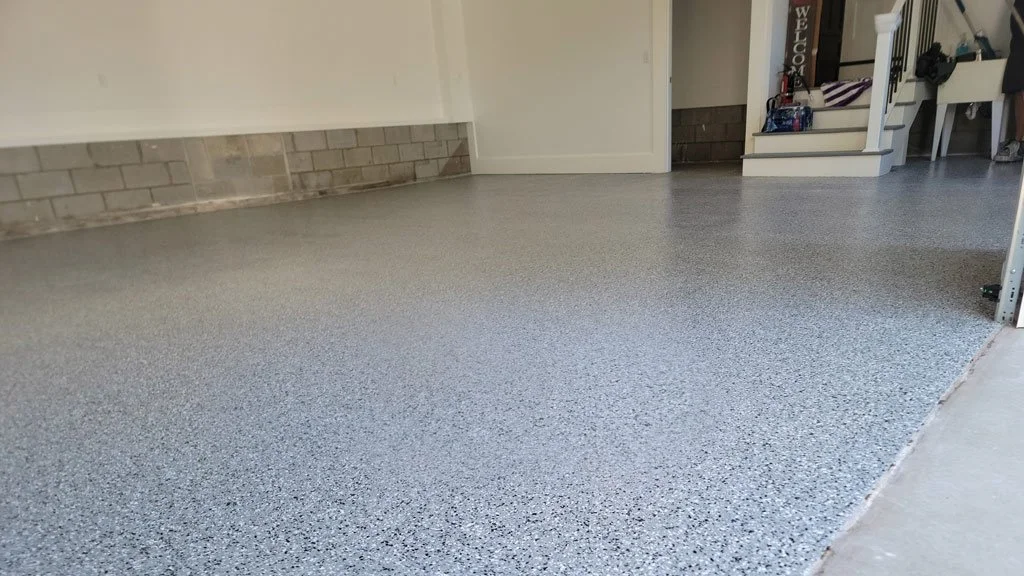 Decorative epoxy garage floor in a home with a brick wall, staircase, and storage corner.