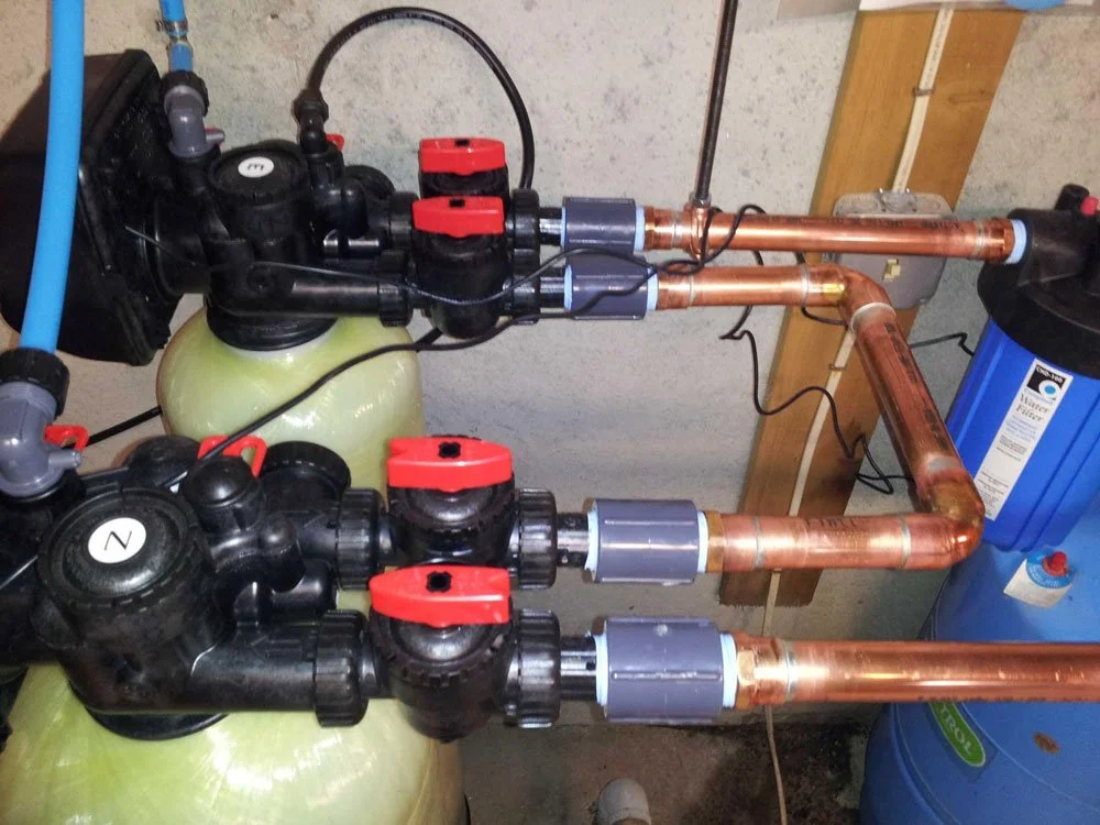 Plumbing system with two large filtration tanks connected to copper pipes and a water softener
