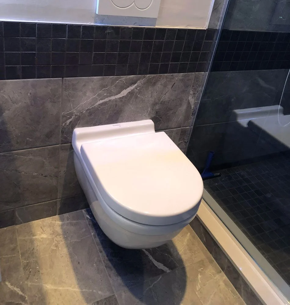 A modern toilet in a bathroom with dark gray tile and a glass shower enclosure.
