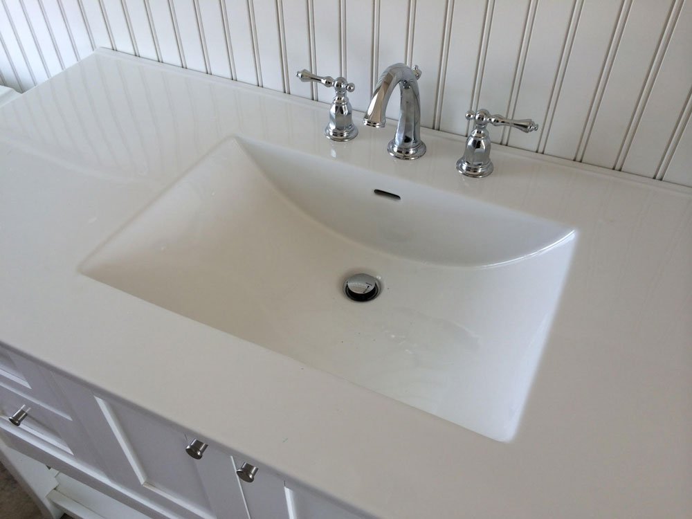 White bathroom sink with silver faucet and handles, mounted on a white vanity with cabinets, against a wall with vertical beadboard paneling.