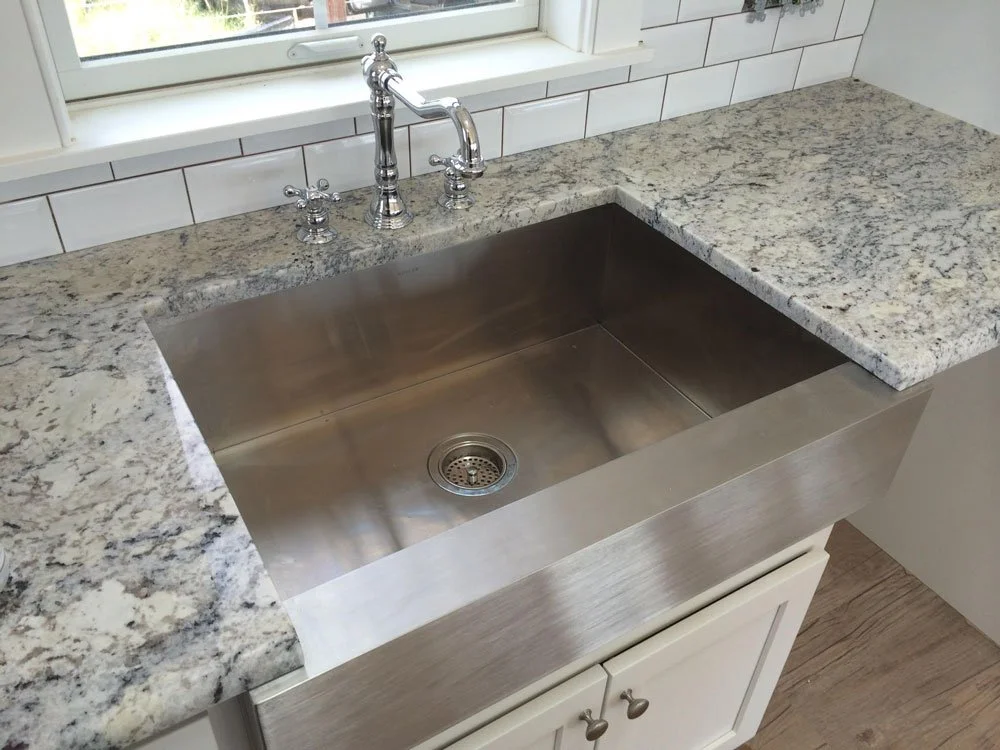 A kitchen sink with a stainless steel basin, granite countertop, and chrome faucet, located below a window.