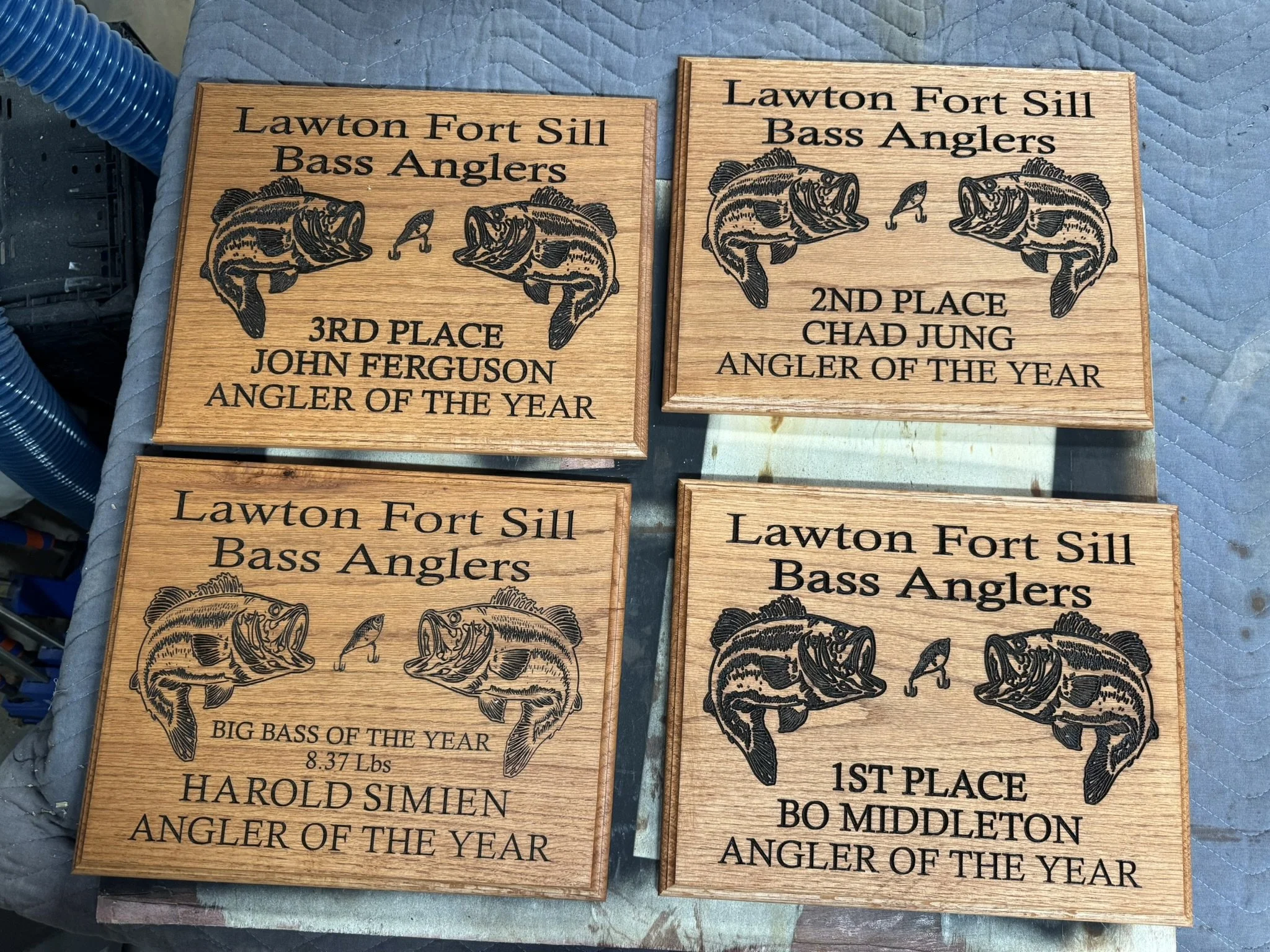 Decorative wooden plaques with engraved fishing-related awards for bass anglers, featuring fish illustrations and award rankings.
