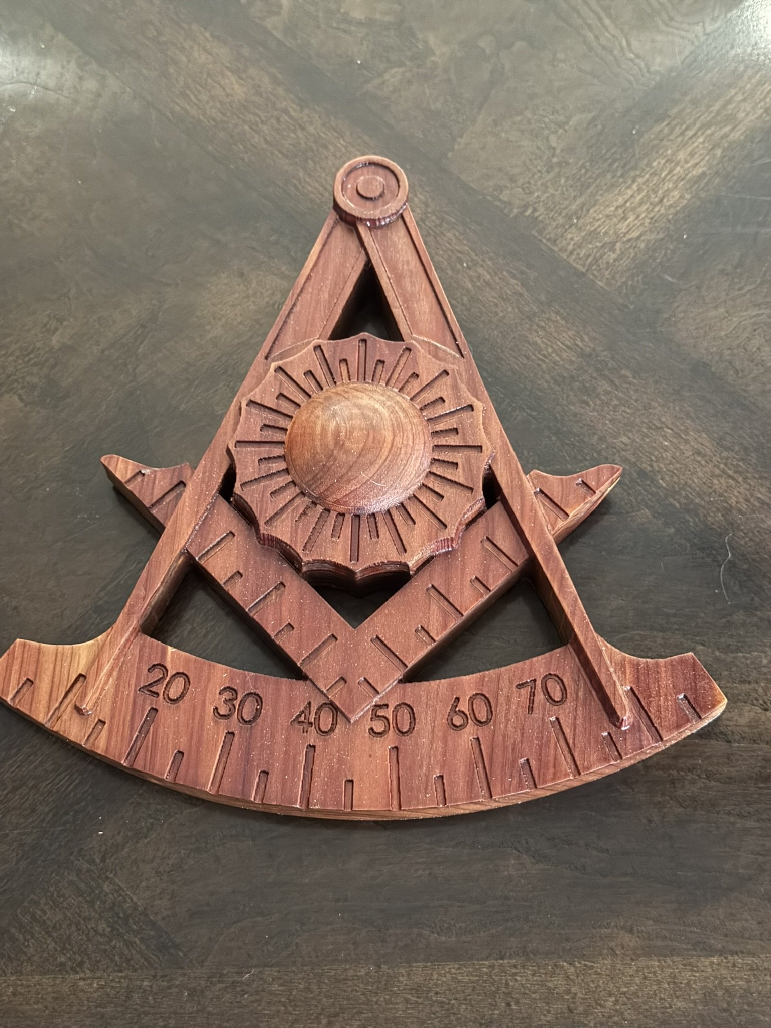 A wooden weather vane with a sun design and degree markings, placed on a dark surface.