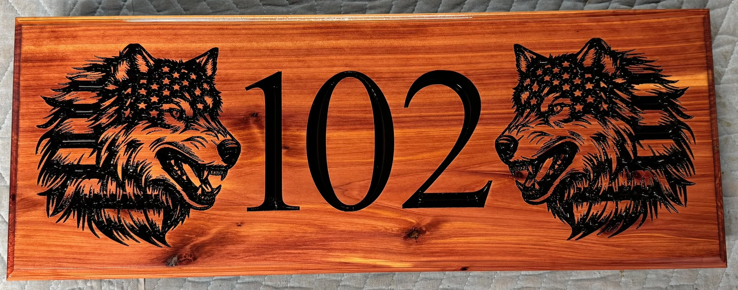 Wooden decorative sign with the number 102 in the center, flanked by two black wolf head silhouettes with star patterns in their fur.