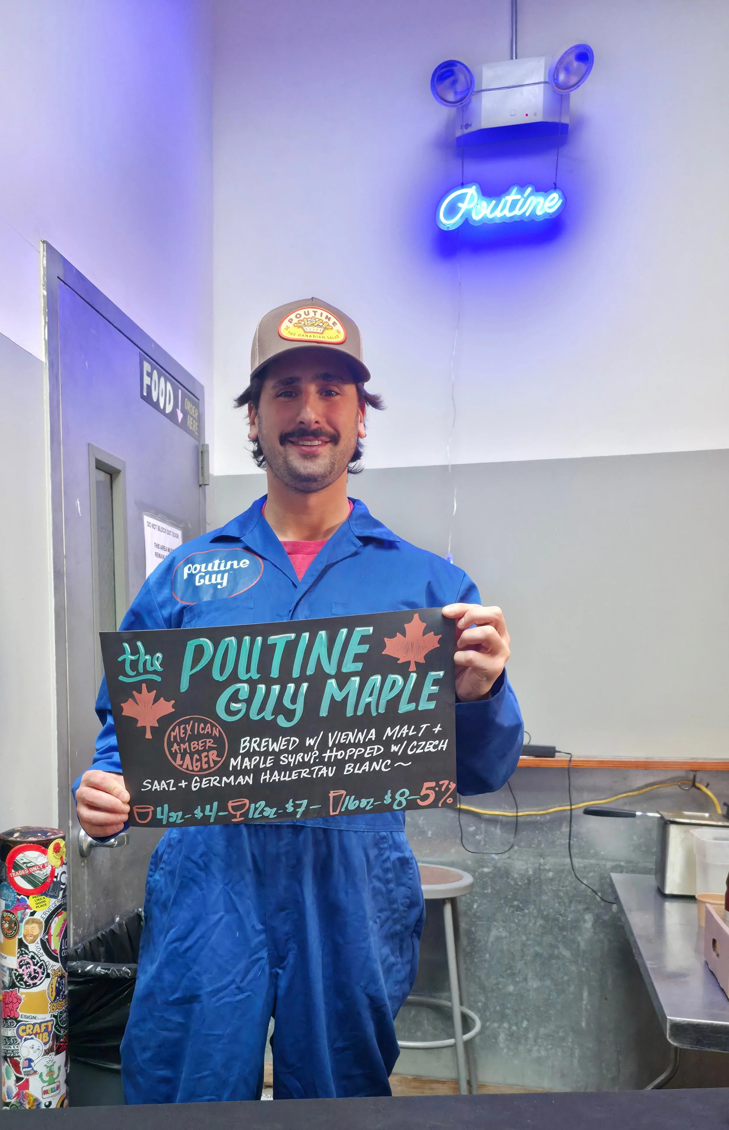 A man with dark hair and a beard in a blue apron and a trucker hat that reads "Poutine Guy" is holding a blackboard menu at a food stand. Behind him, there is a wall with a neon sign that reads "Poutine" and a wall-mounted speaker with two blue lights.