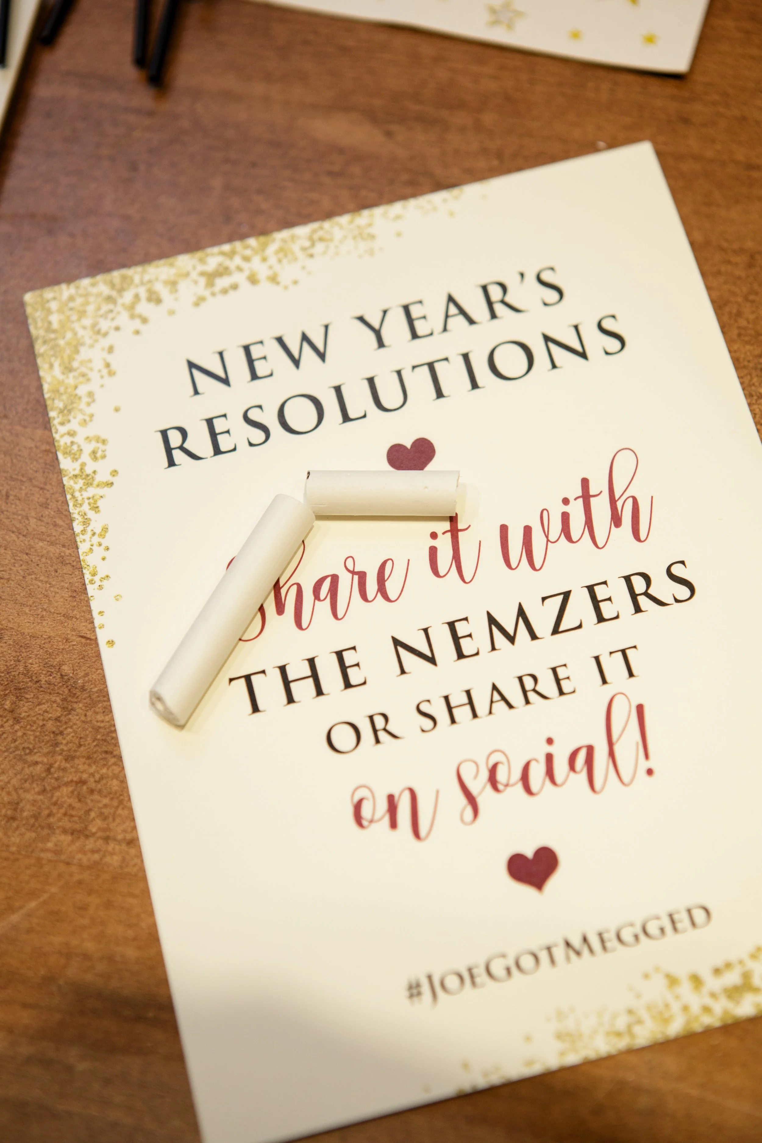 A festive holiday card with gold glitter accents and red hearts, featuring a message about New Year's resolutions to share on social media.
