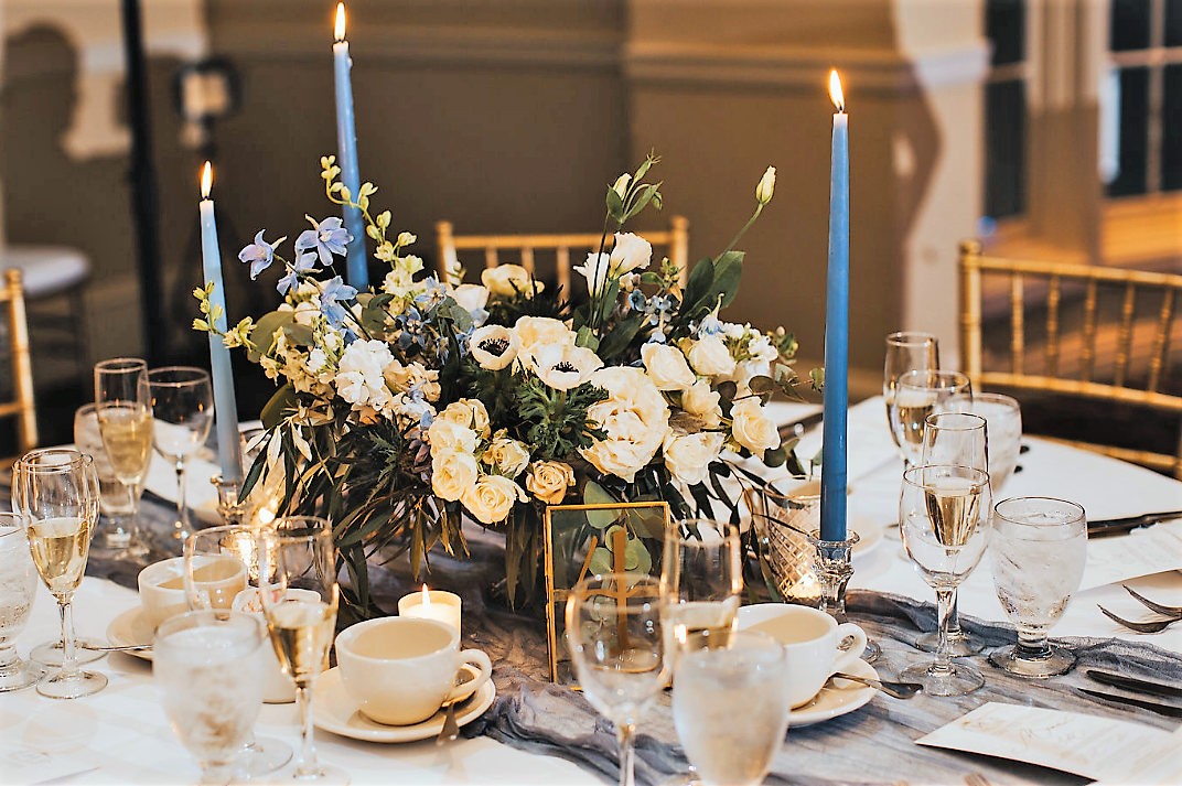 Elegant dining table with a flower centerpiece, candles, and blue taper candles, set for a formal event.