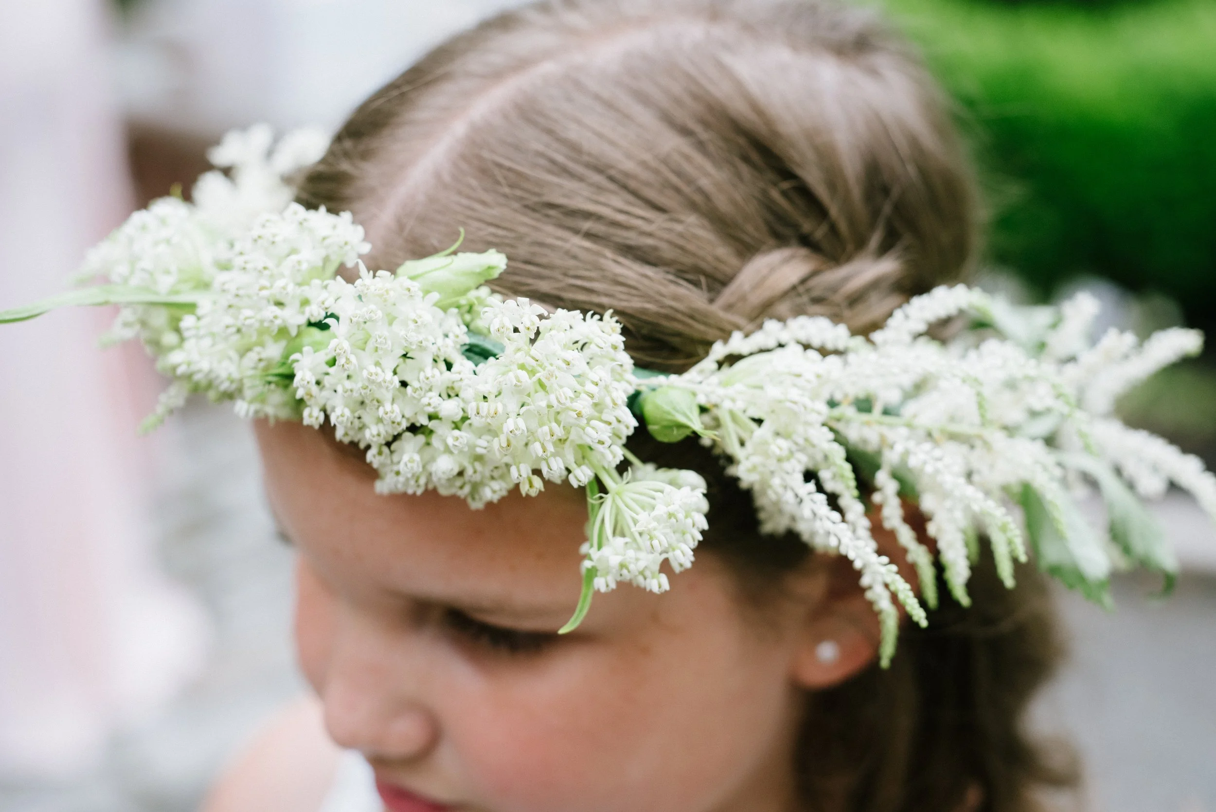 A person with brown hair wearing a floral crown made of white flowers.
