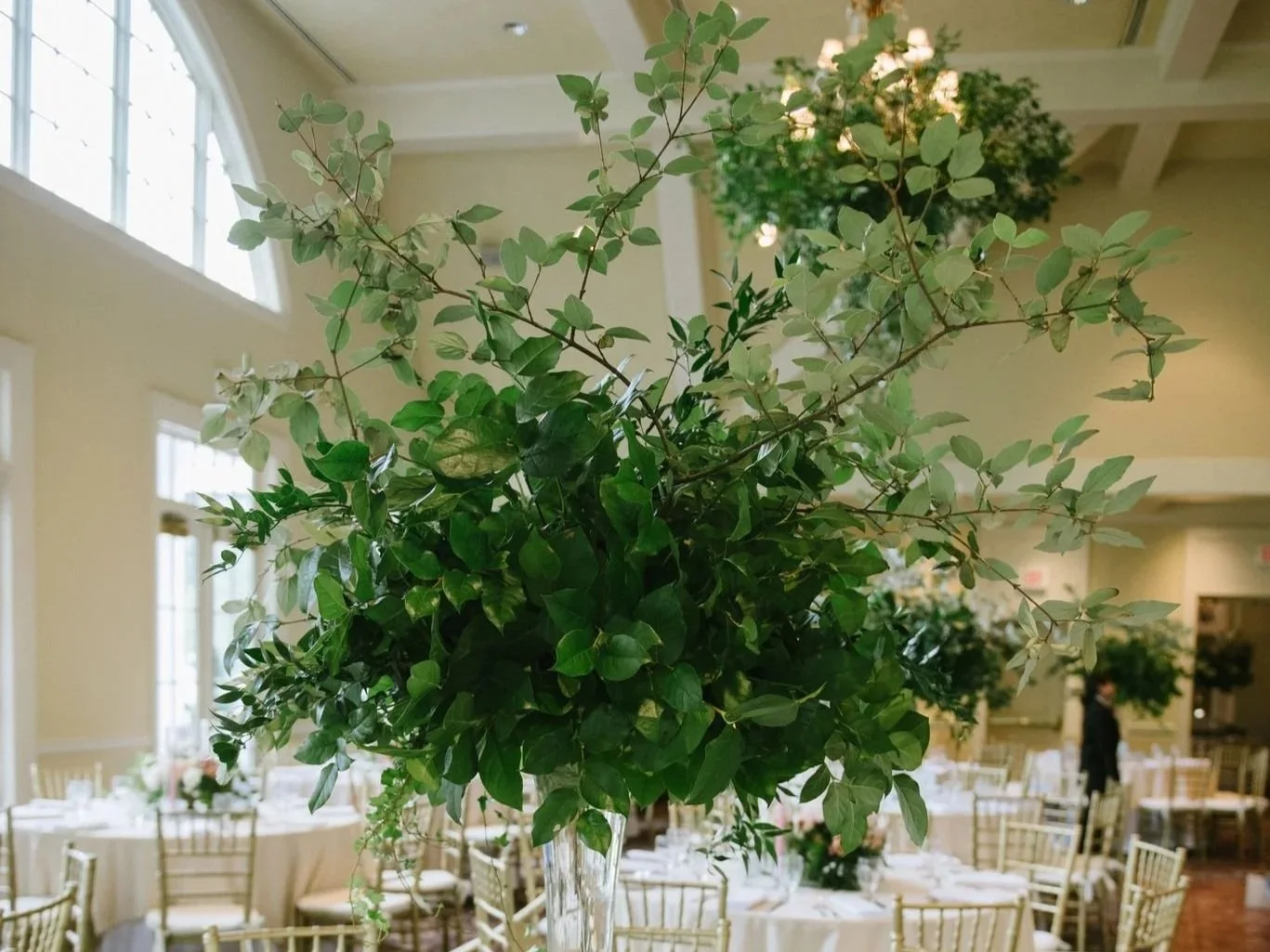 Foliage centerpiece in a decorated banquet hall with tables and chairs.