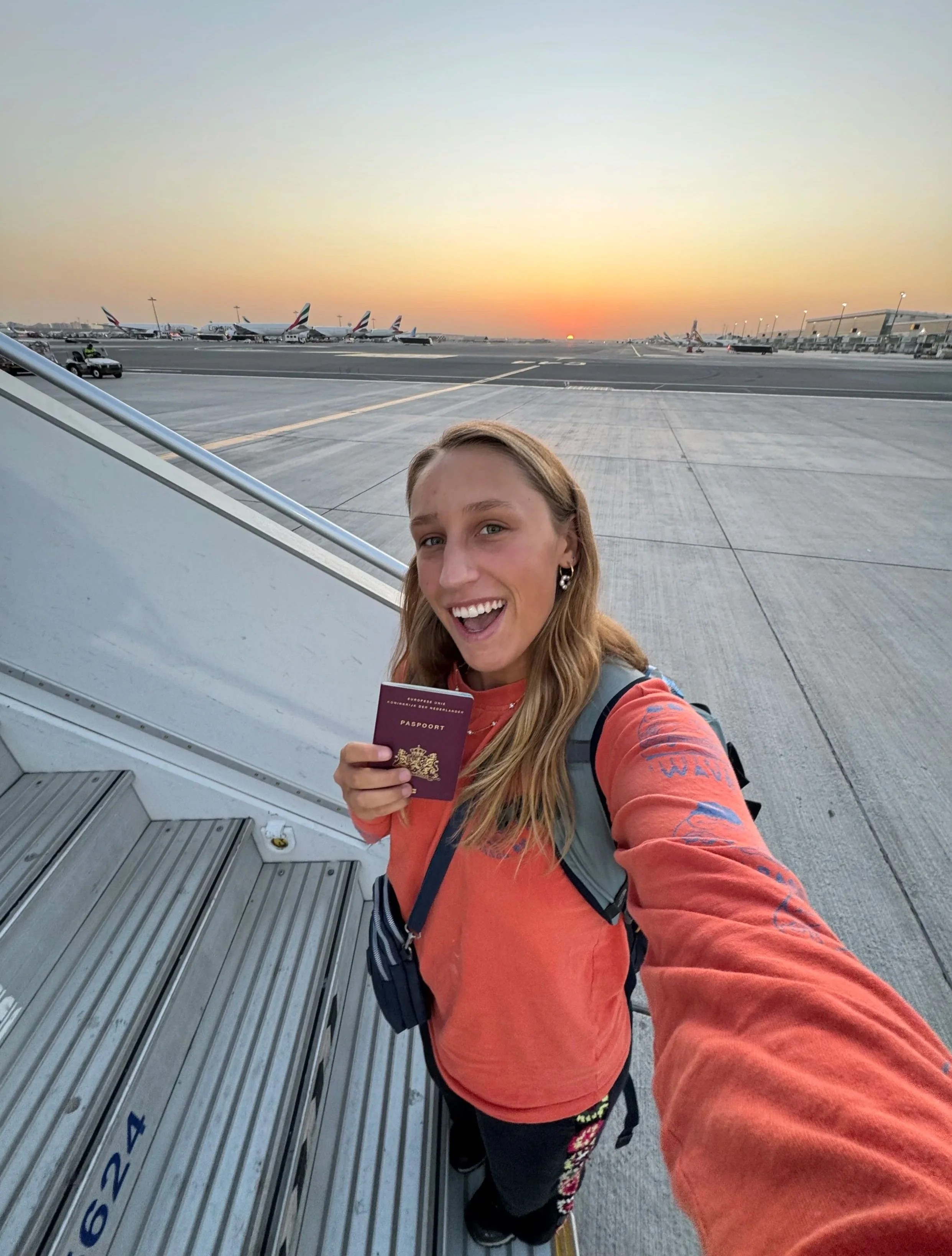 Lara on an airplane tarmac holding a passport, with airplanes parked in the background at sunset in Sri Lanka.