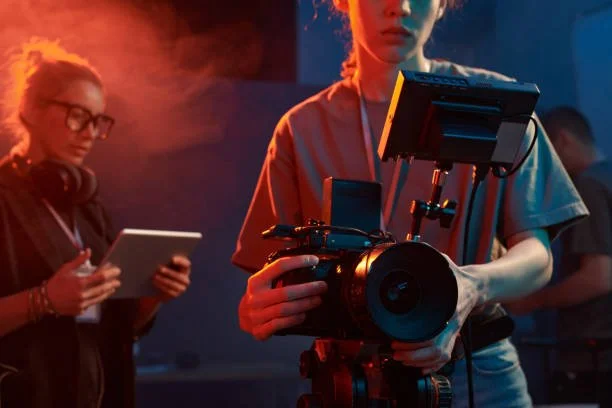 Person operating professional film camera on set with crew members in the background.