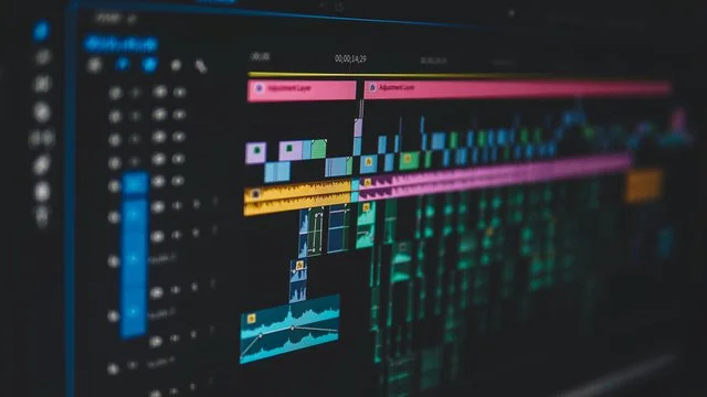 Computer screen displaying a video editing timeline with colorful tracks, clips, and audio waveforms on a dark background.