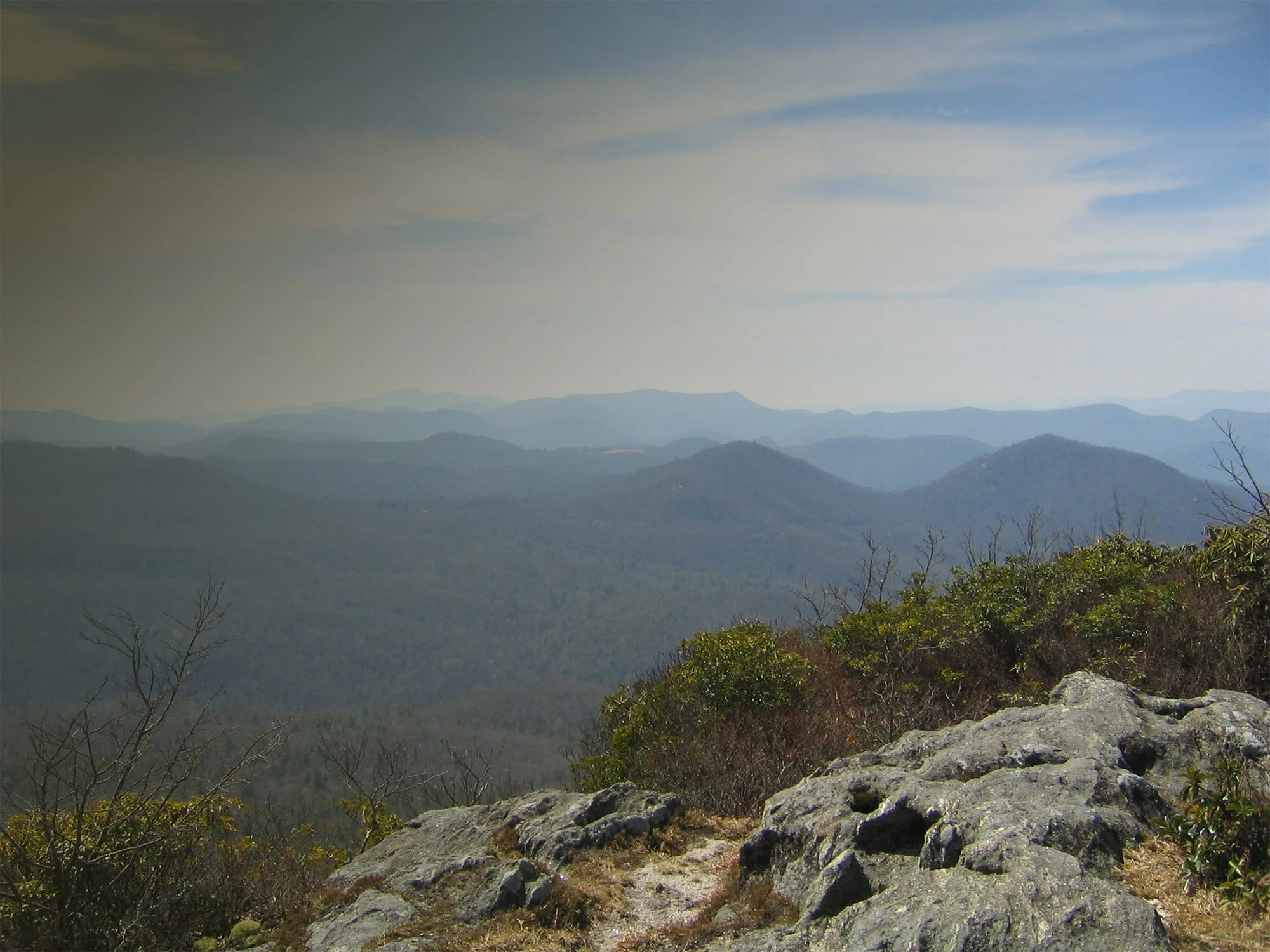 Scenic view of layered mountain ridges under a partly cloudy sky, with some rocks and sparse vegetation in the foreground.