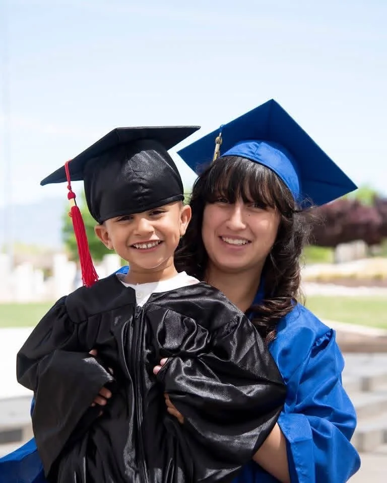 Young boy and woman in graduation caps and gowns celebrating outdoors.